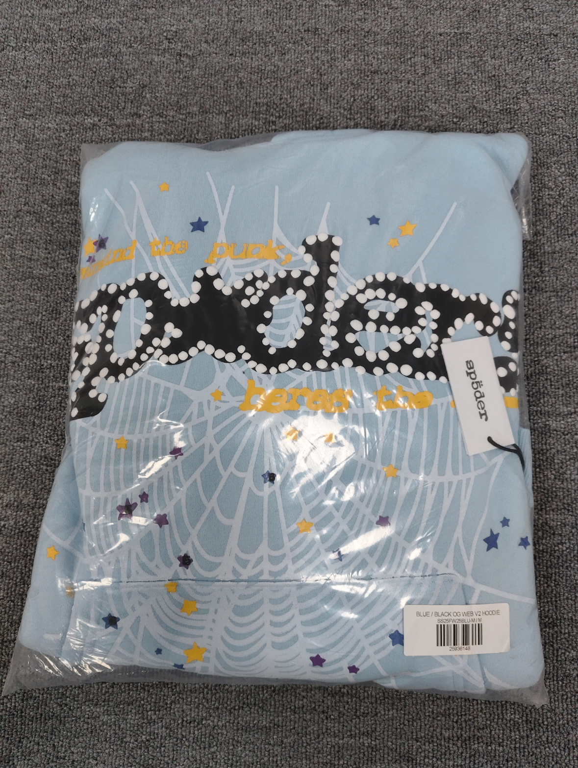 a light blue Sp5der Worldwide hoodie featuring a prominent black graphic logo and a white spiderweb design filled with colorful stars