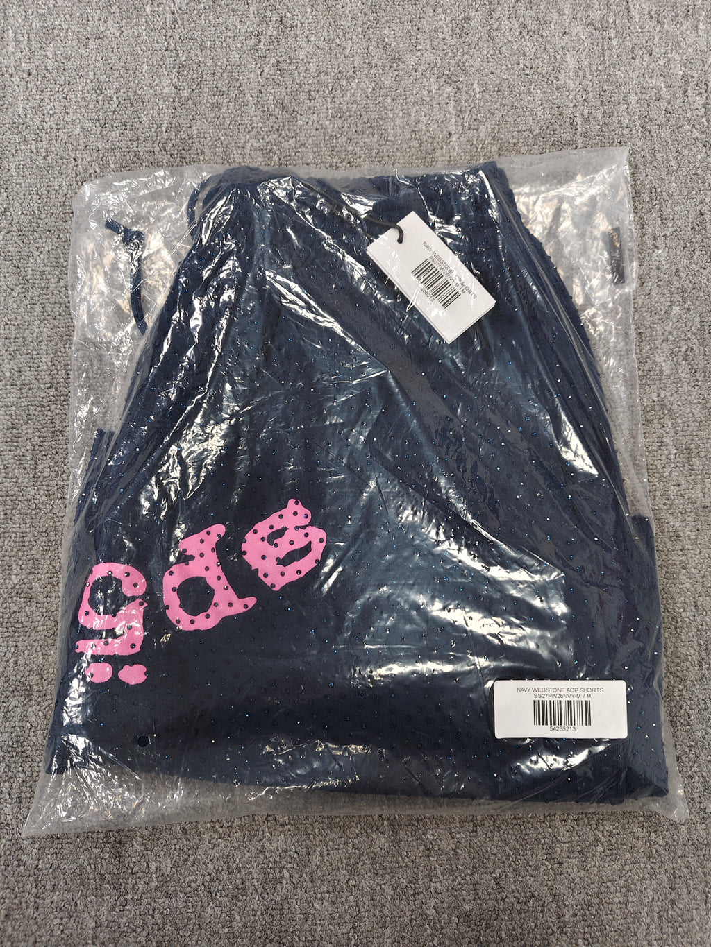 Sp5der jogger shorts are a navy blue color with a pink text graphic and rhinestone details
