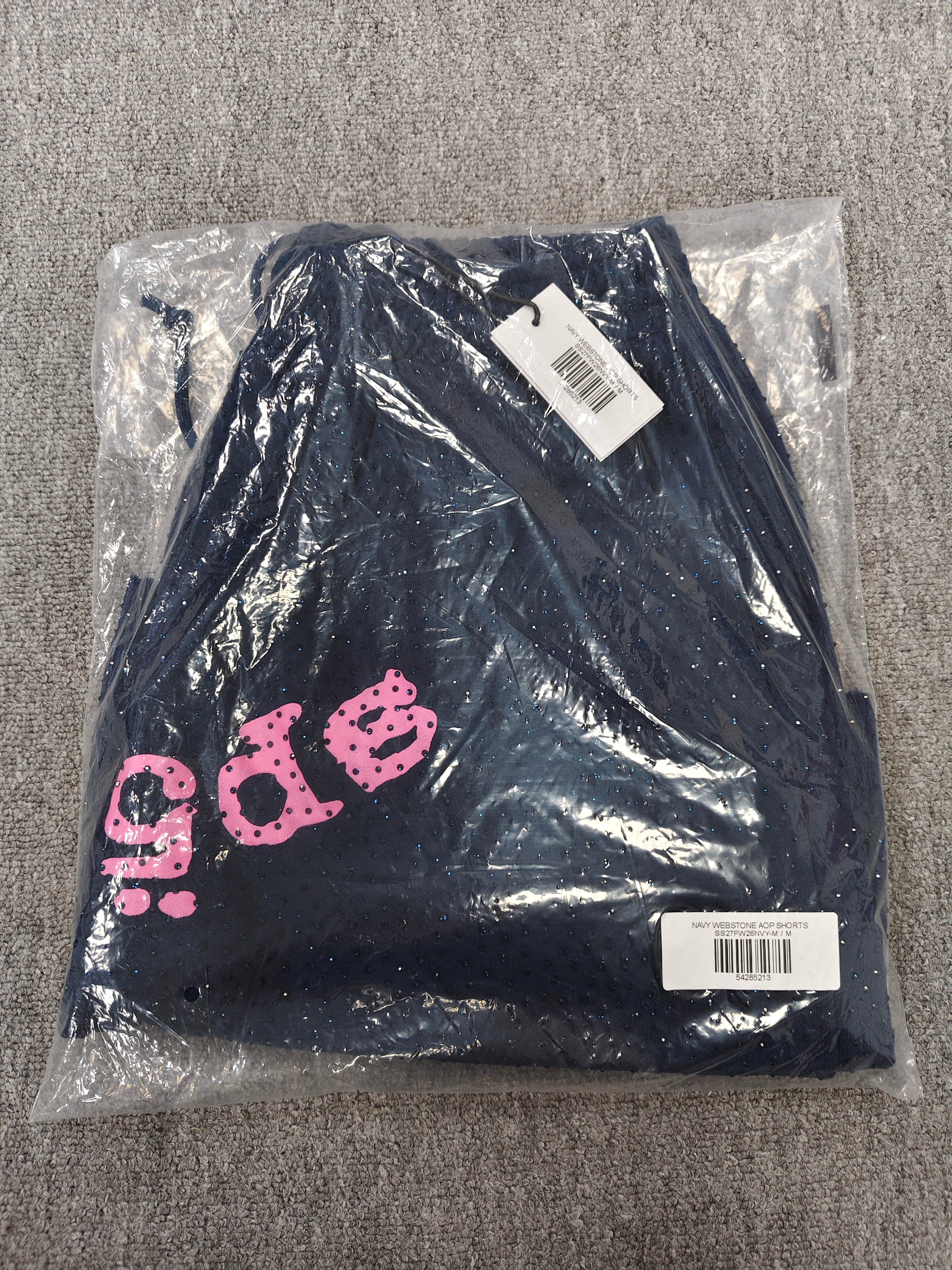 Sp5der jogger shorts are a navy blue color with a pink text graphic and rhinestone details