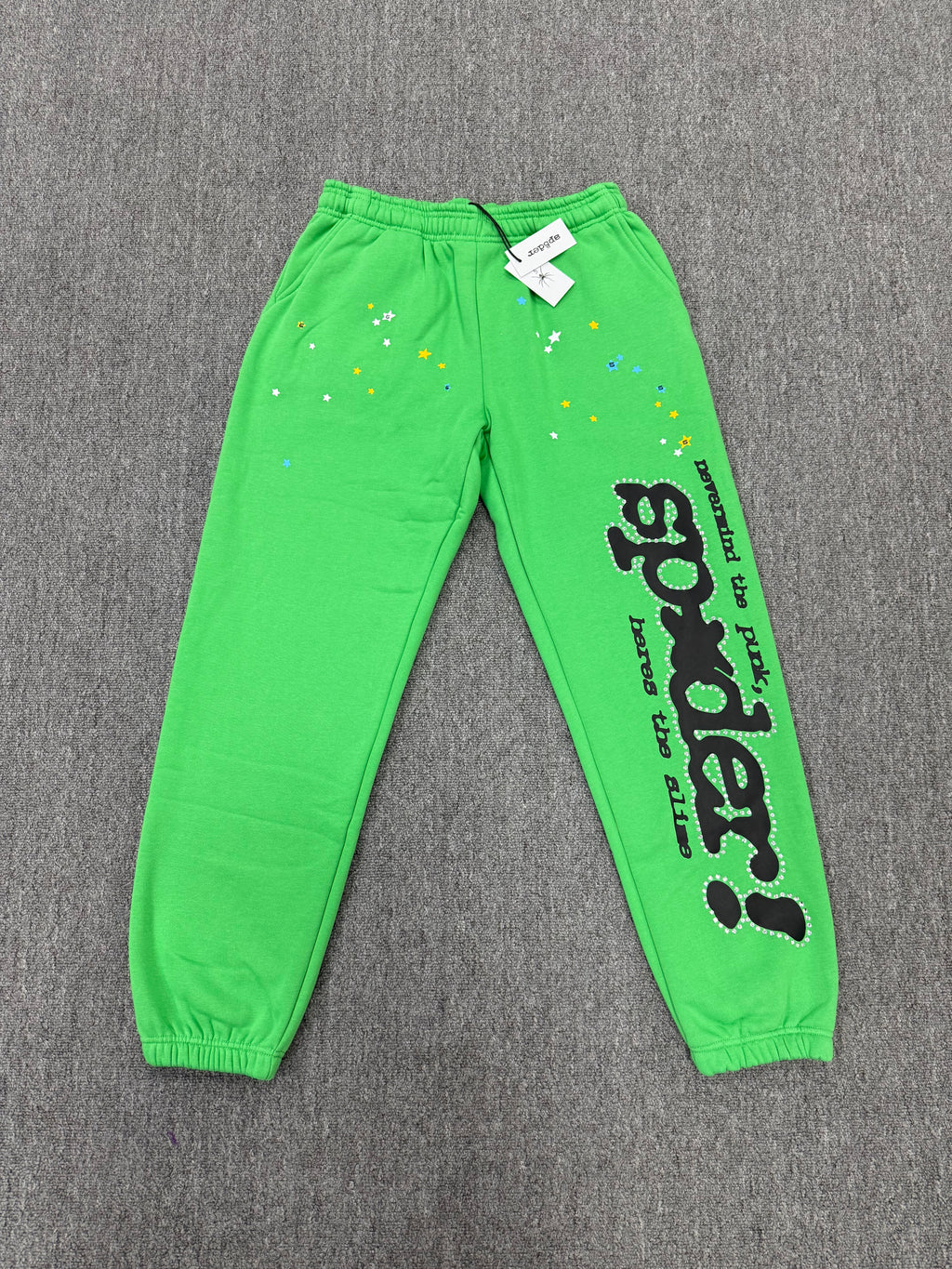 Sp5der Punk V2 Rhinestone track pants in green, featuring prominent black rhinestone-lined graphics and stars