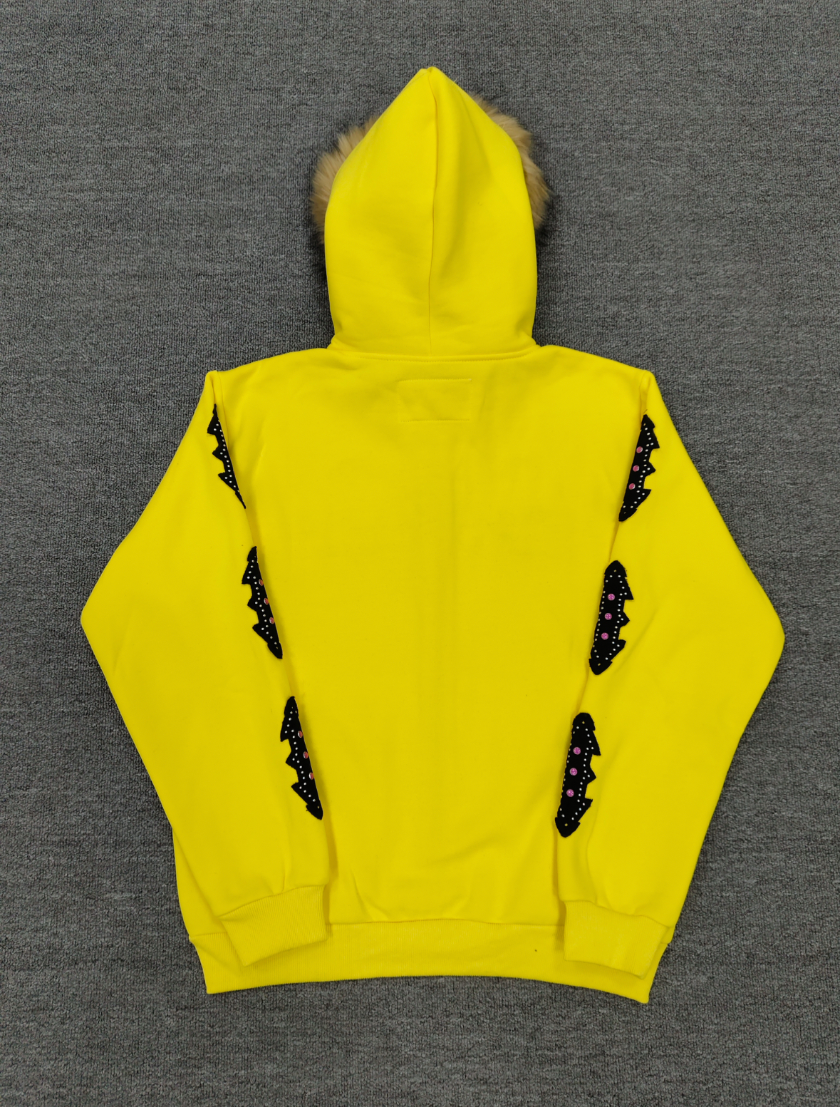 a yellow Sp5der fur-hooded zip-up sweatshirt featuring a prominent black logo and studded sleeve details