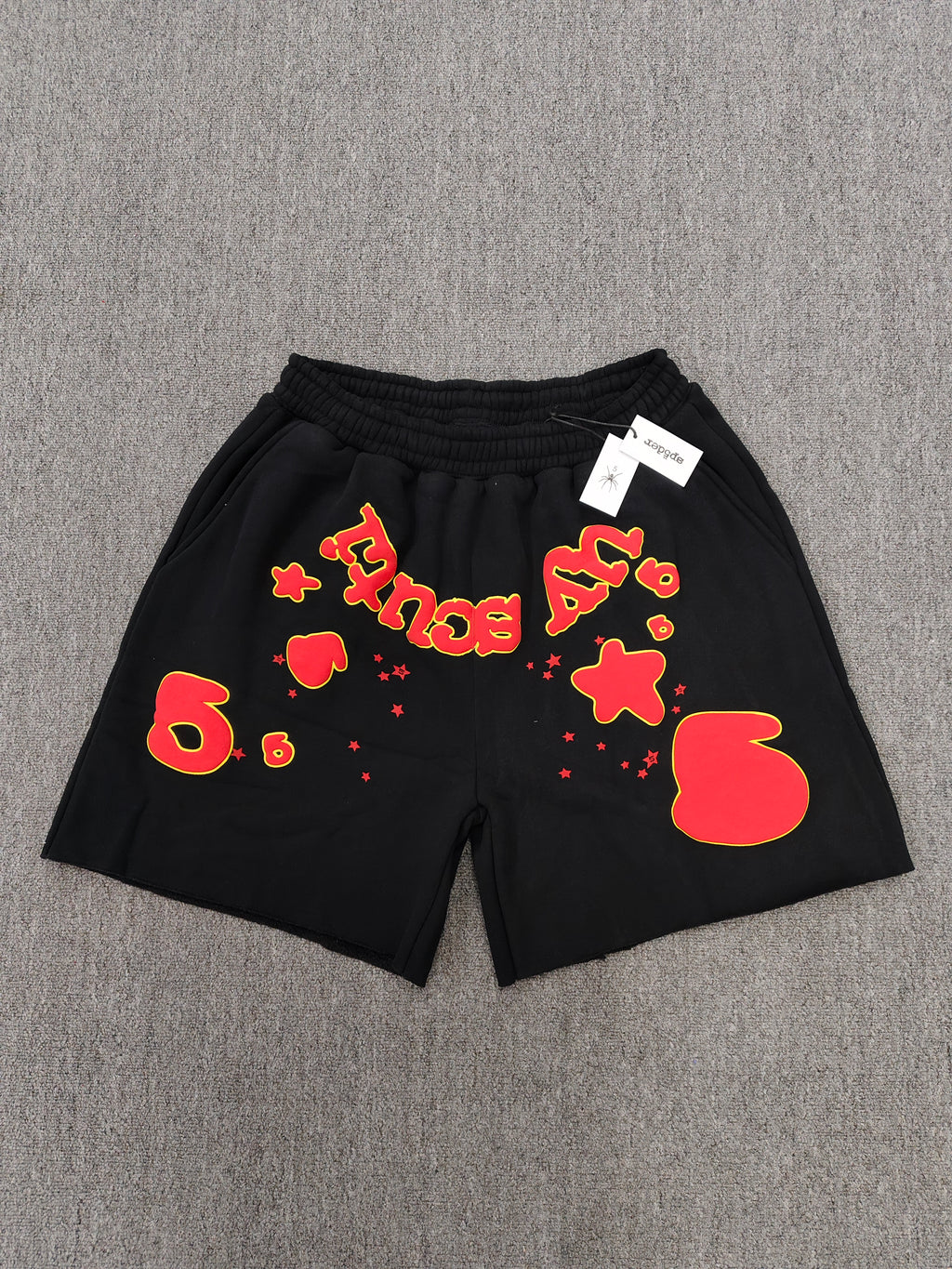 Sp5der x UY SCUTI collaboration shorts featuring bold red graphic logos on a black base