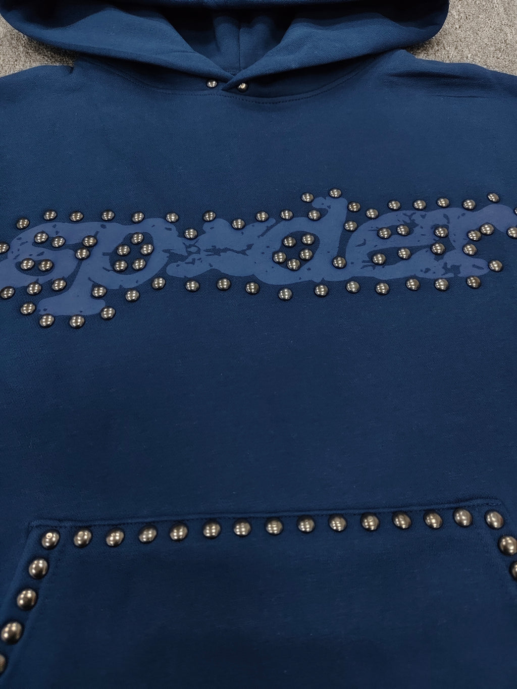 a blue Sp5der Punk V3 Studded Hoodie, featuring rhinestone-accented branding and silver stud details along the hood, logo, and pocket
