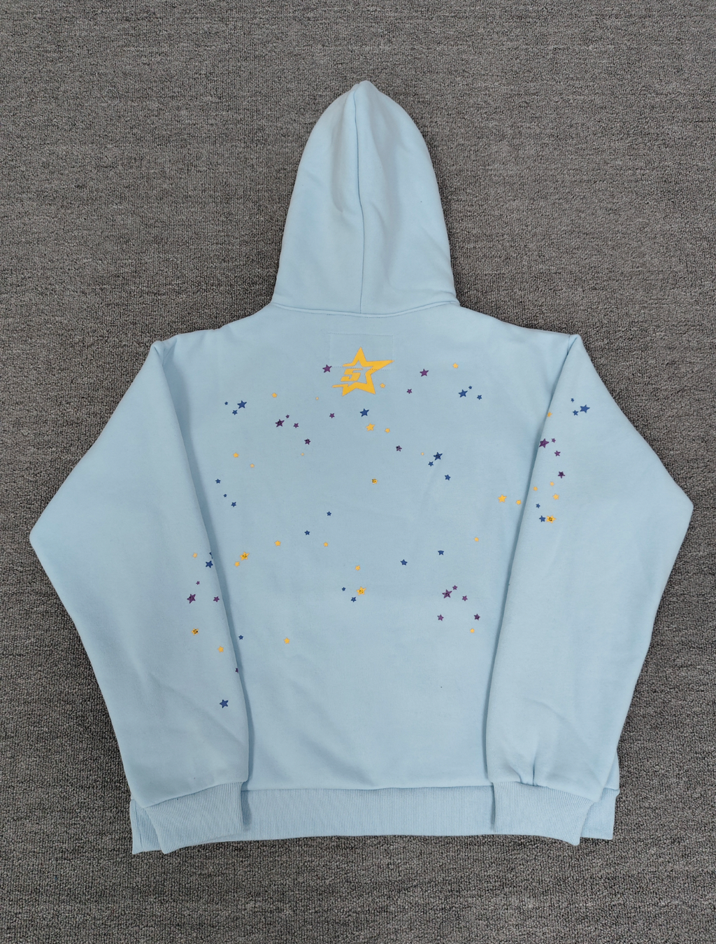 a light blue Sp5der Worldwide hoodie featuring a prominent black graphic logo and a white spiderweb design filled with colorful stars