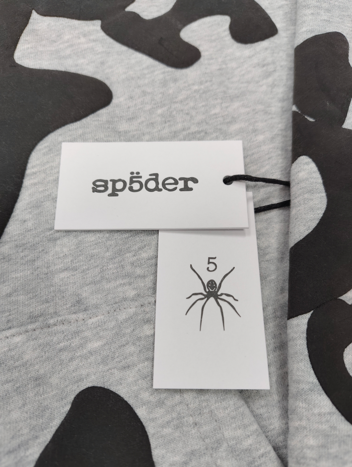 Sp5der Worldwide Beluga hoodie features a distinctive black star graphic across the chest on a light grey heather fabric