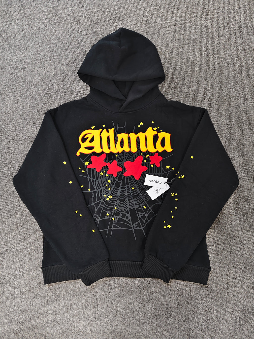 black SP5DER Atlanta hoodie features yellow lettering, red stars, and a spiderweb graphic