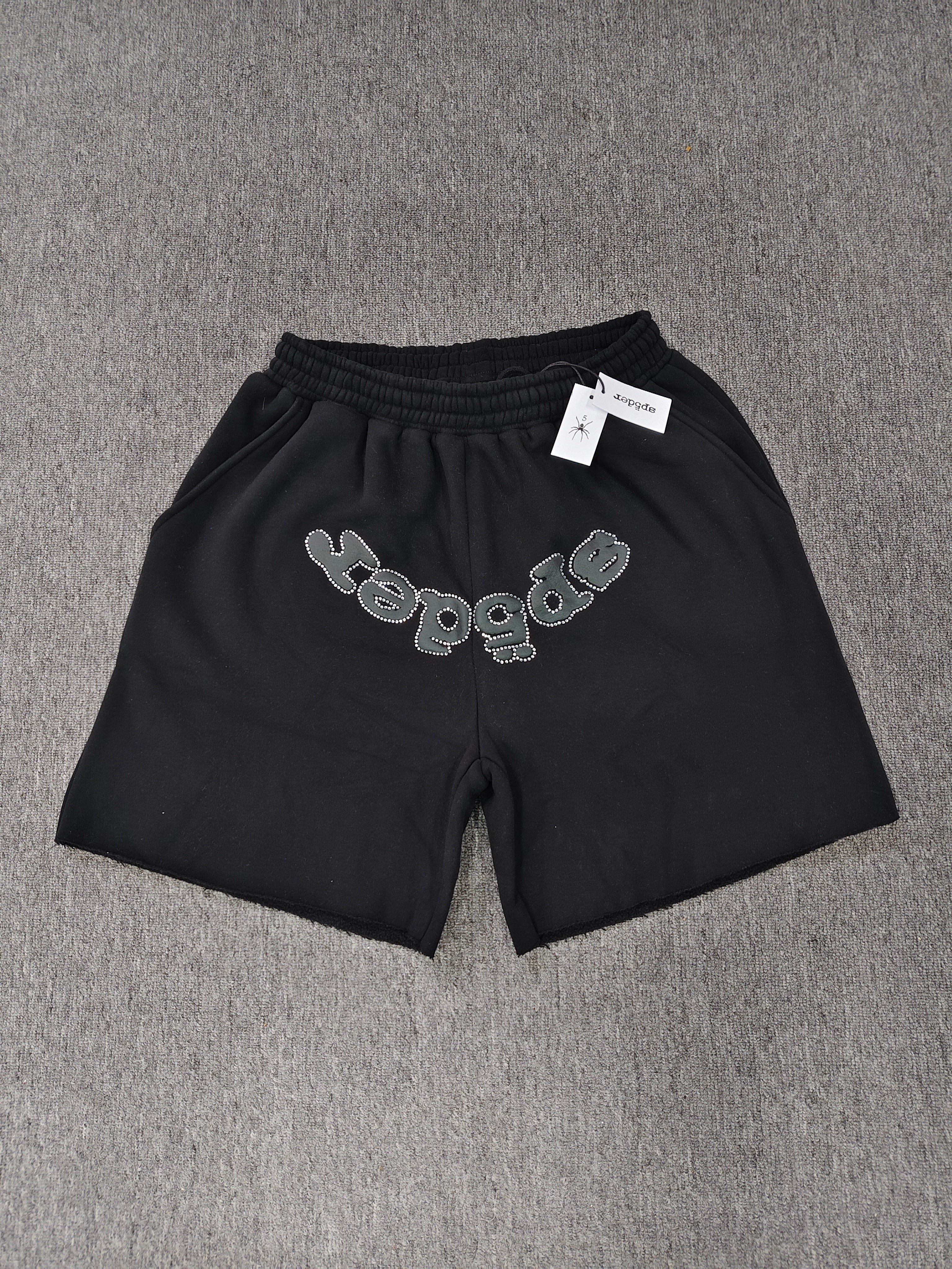 black Sp5der shorts feature a rhinestone-embellished logo and a spider web graphic