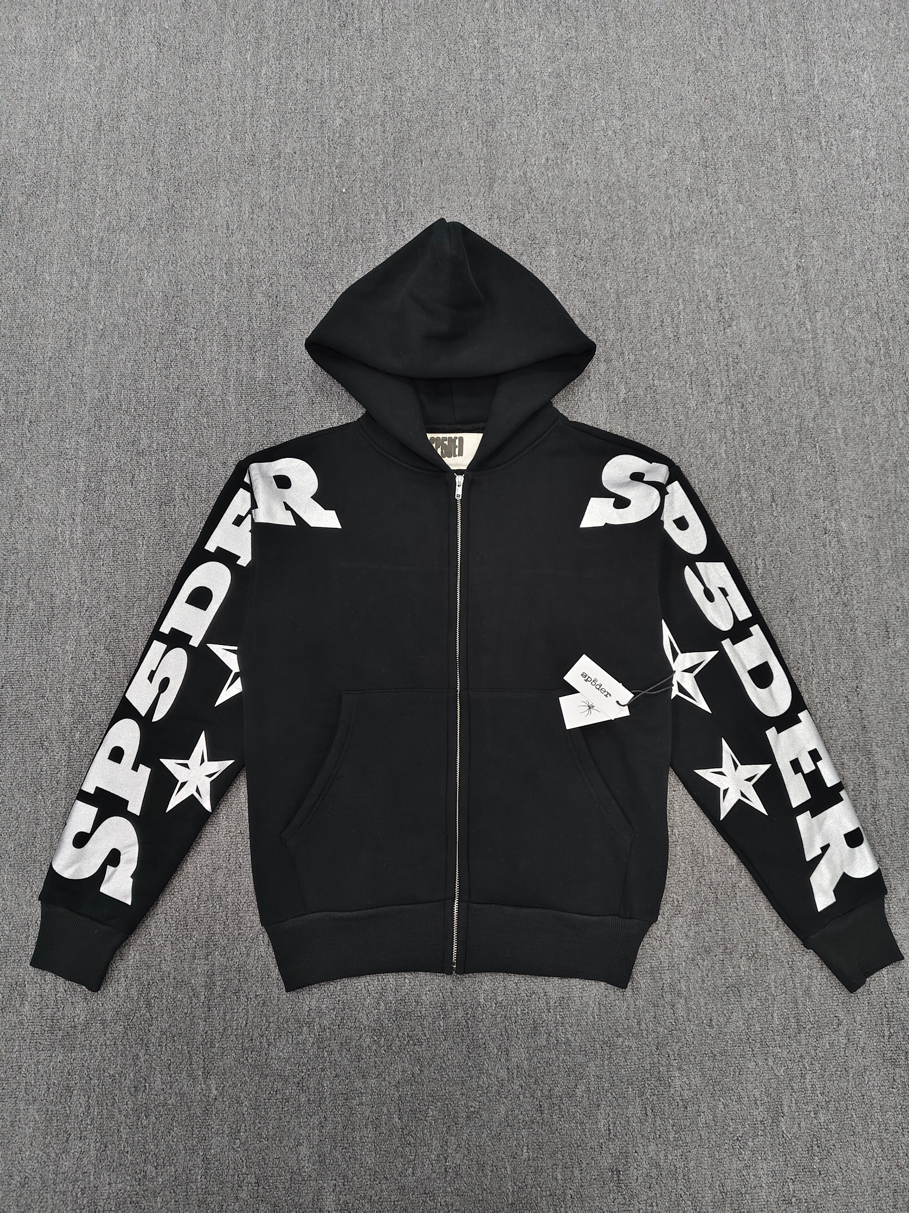 a Sp5der MX555 Zip Hoodie in black, featuring white graphic lettering and star prints on the sleeves