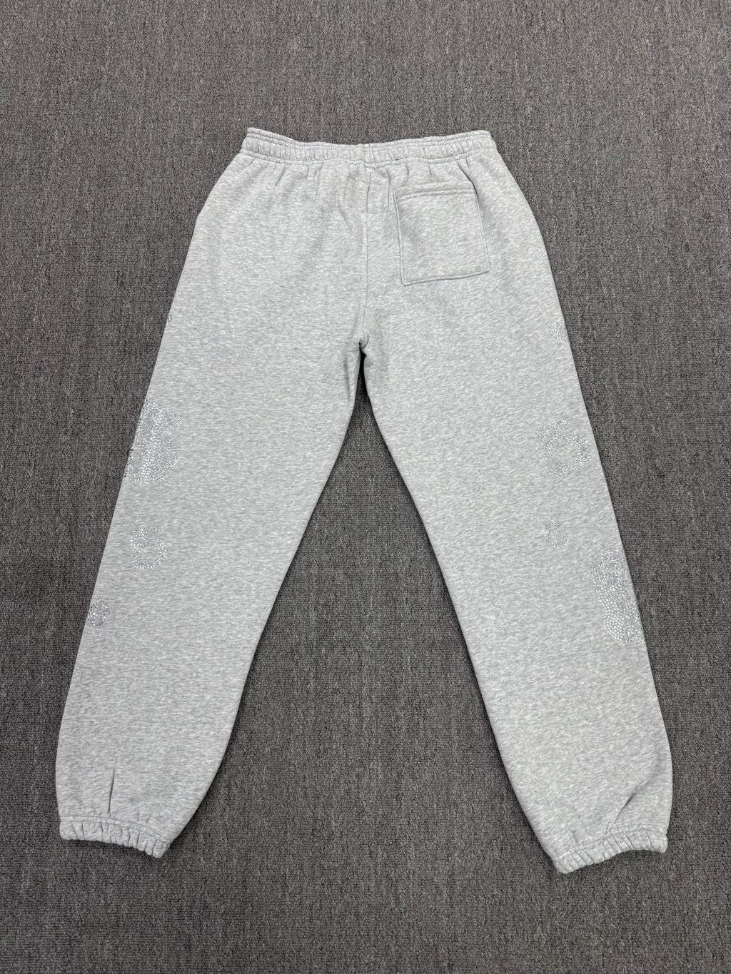 light grey sp5der joggers feature a unique rhinestone across the front hip area
