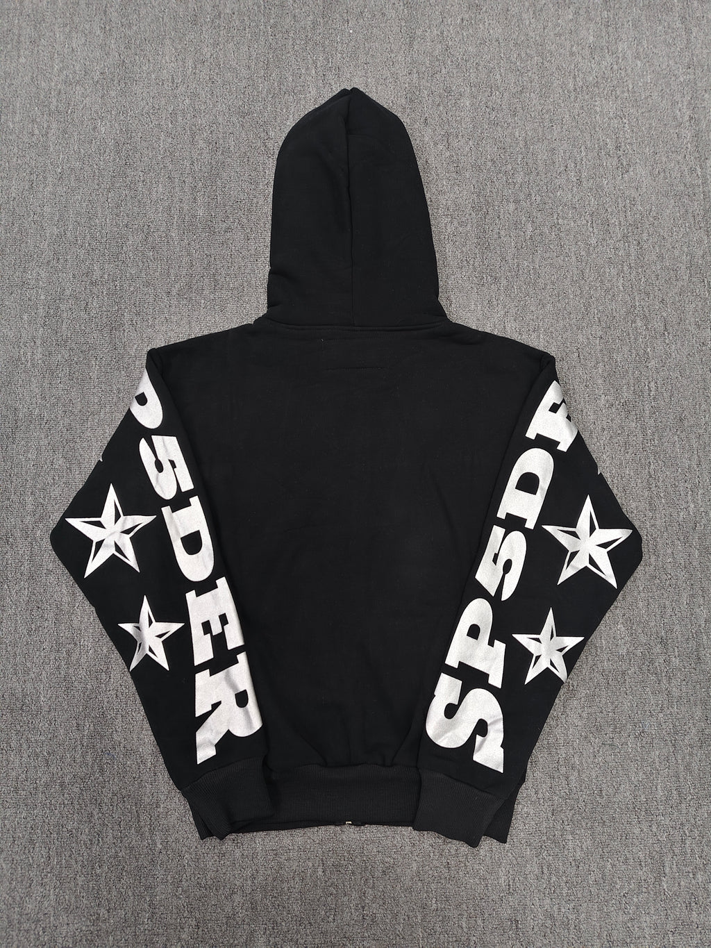 a Sp5der MX555 Zip Hoodie in black, featuring white graphic lettering and star prints on the sleeves