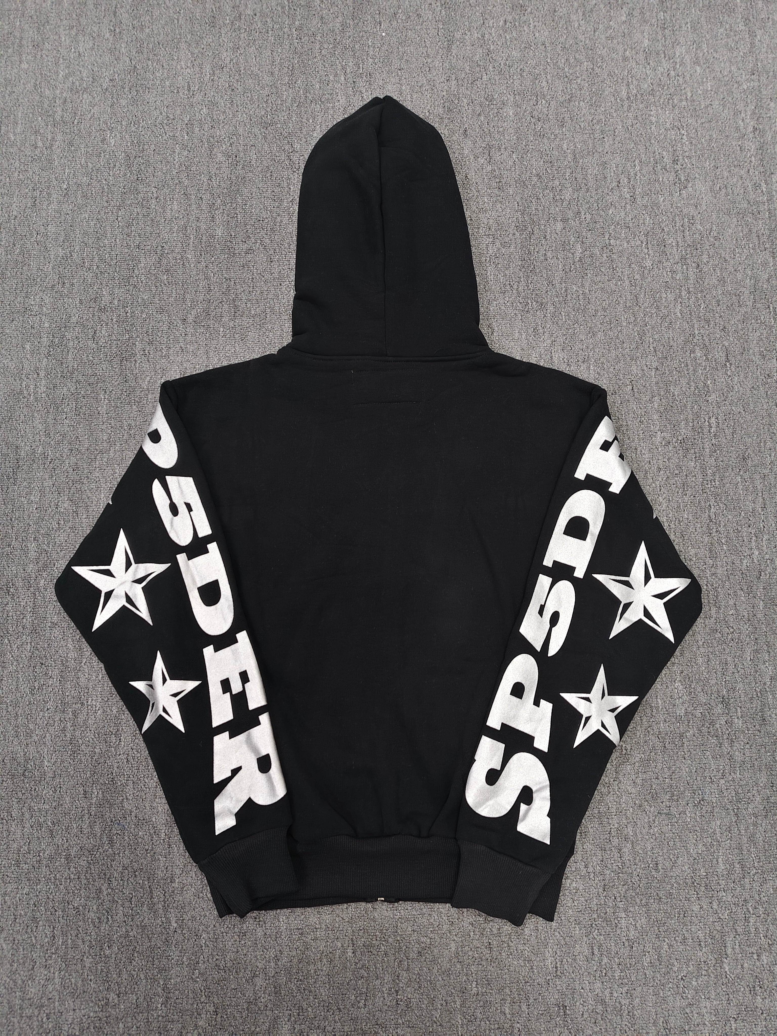 a Sp5der MX555 Zip Hoodie in black, featuring white graphic lettering and star prints on the sleeves