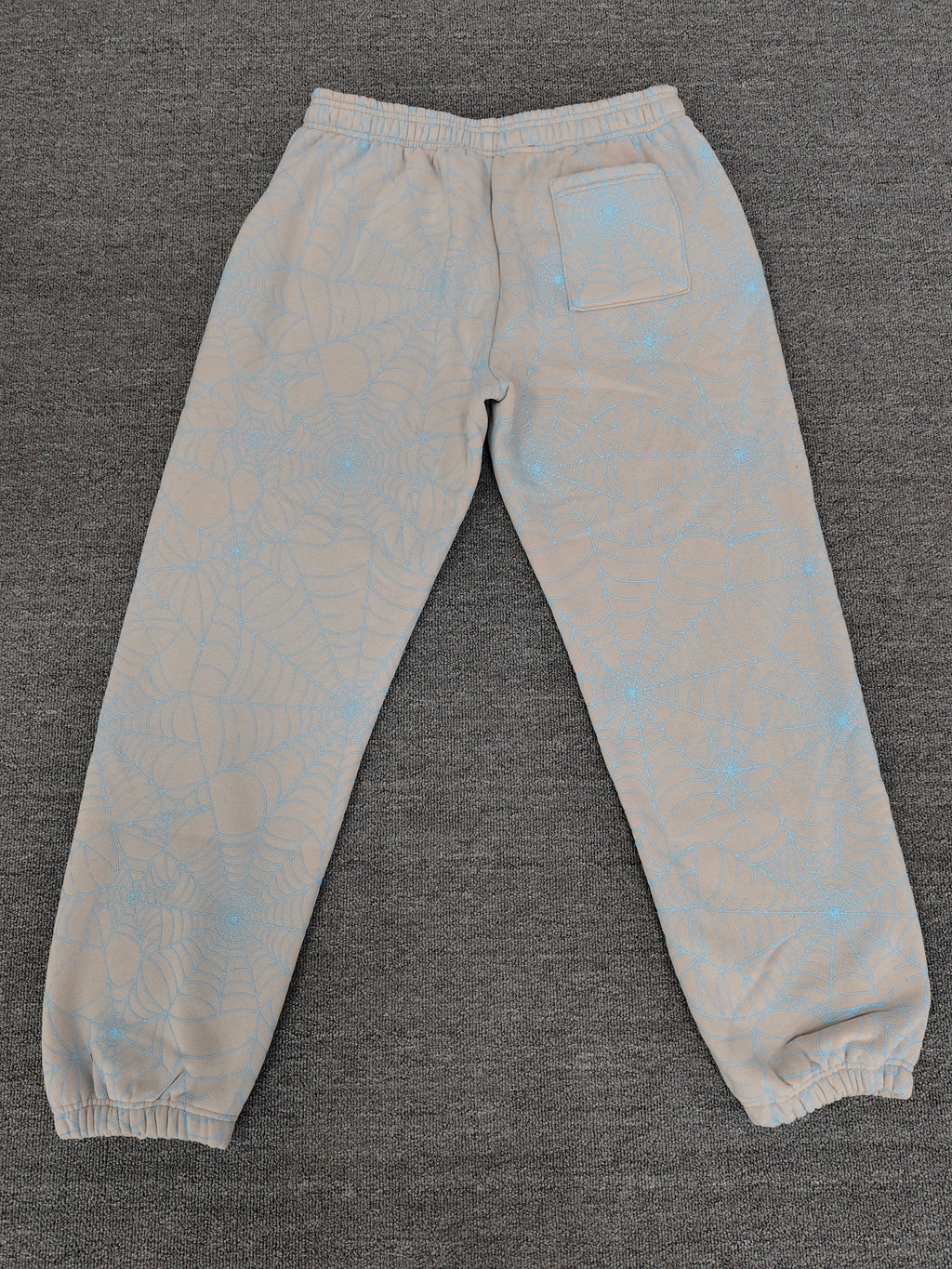 Sp5der AOP Web Heather Grey Sweatpants featuring a distinctive all-over blue spiderweb print and a contrasting black logo on the thigh.