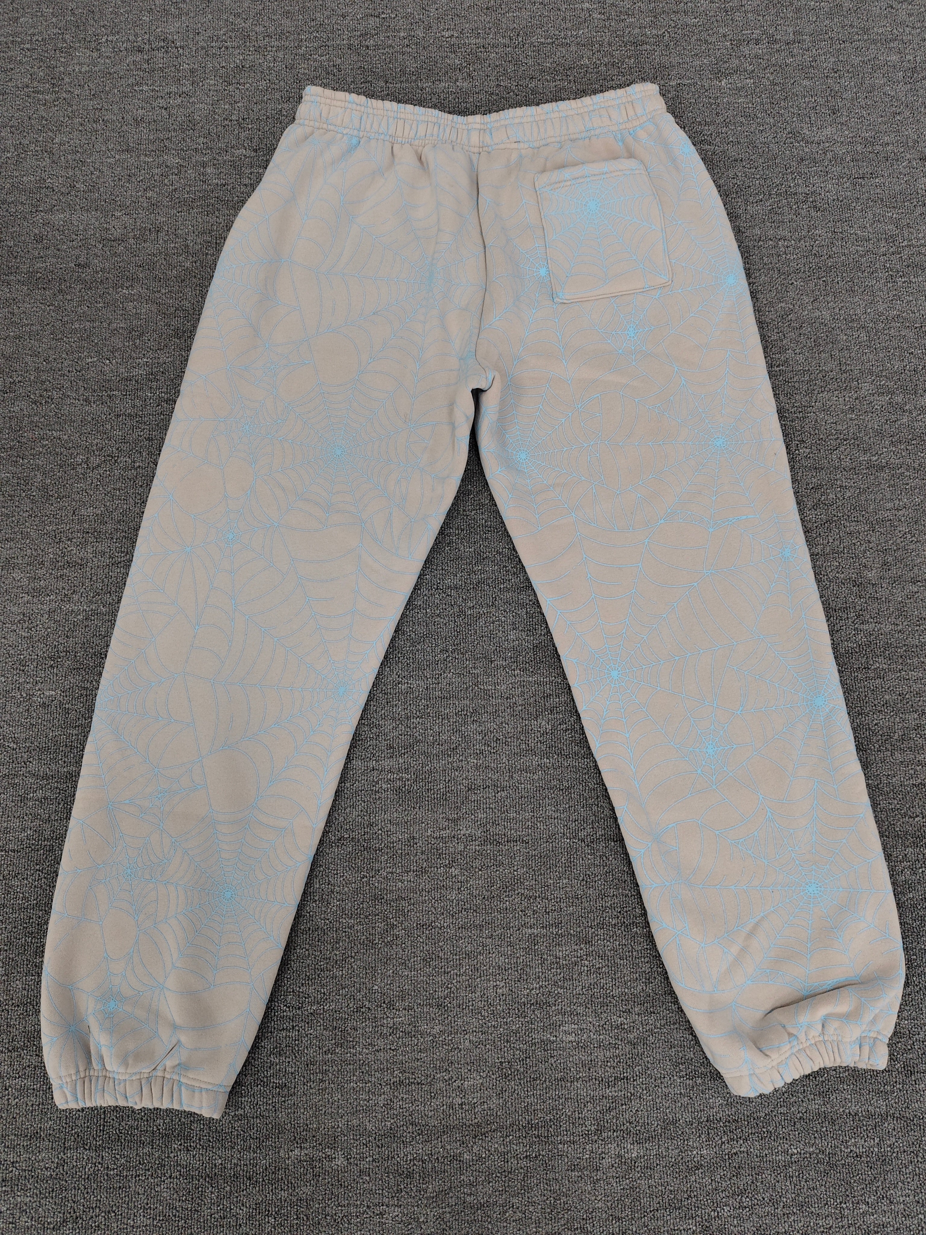 Sp5der AOP Web Heather Grey Sweatpants featuring a distinctive all-over blue spiderweb print and a contrasting black logo on the thigh.