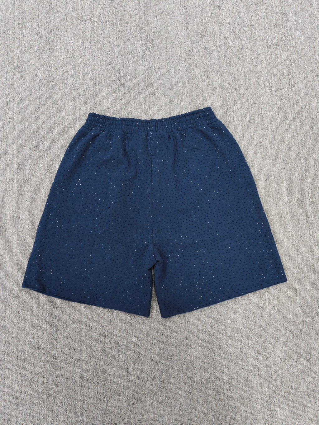 Sp5der jogger shorts are a navy blue color with a pink text graphic and rhinestone details