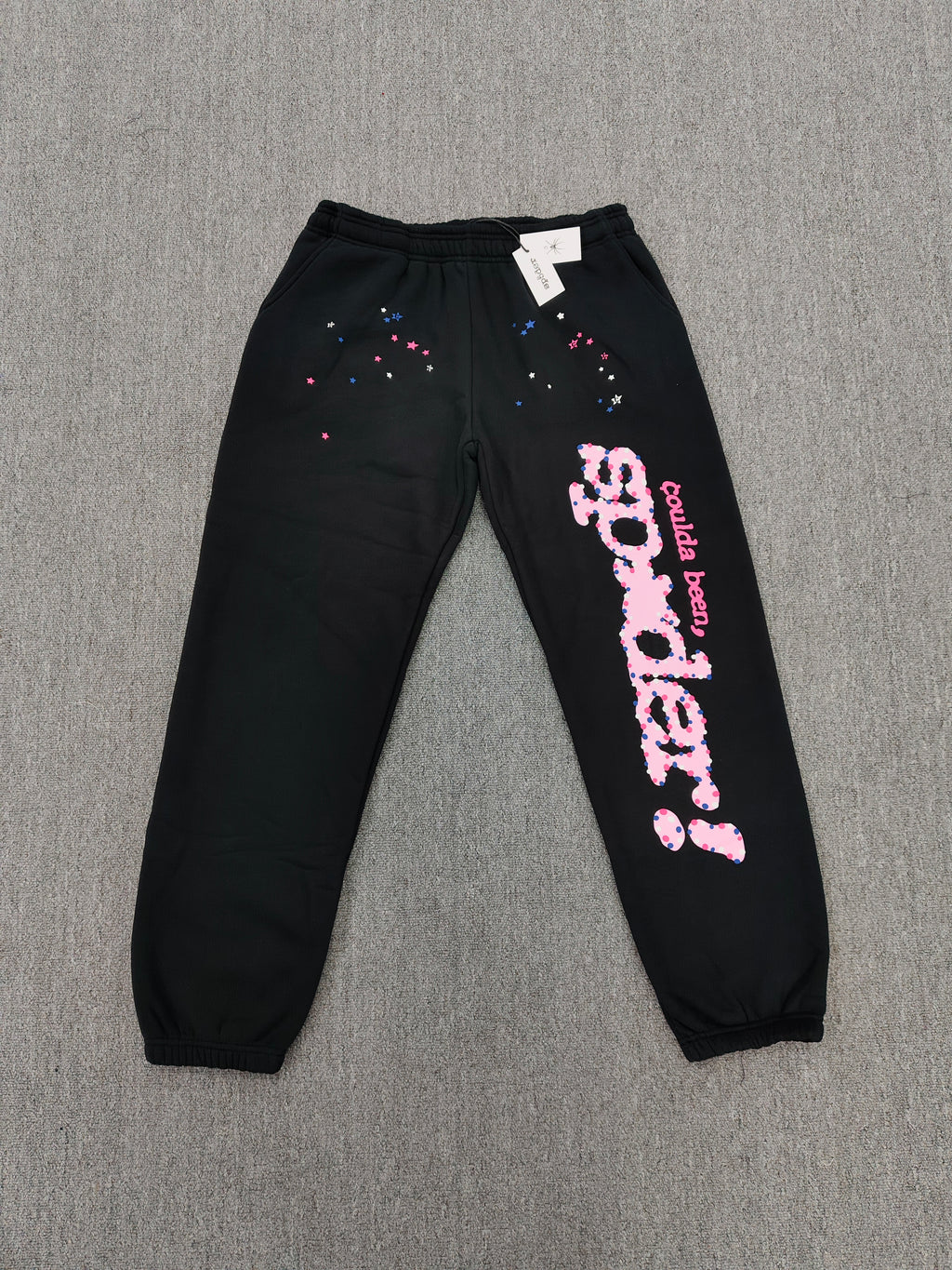 black Sp5der x Coulda Been sweatpants featuring a prominent pink "spider!" graphic and multi-colored star embroidery