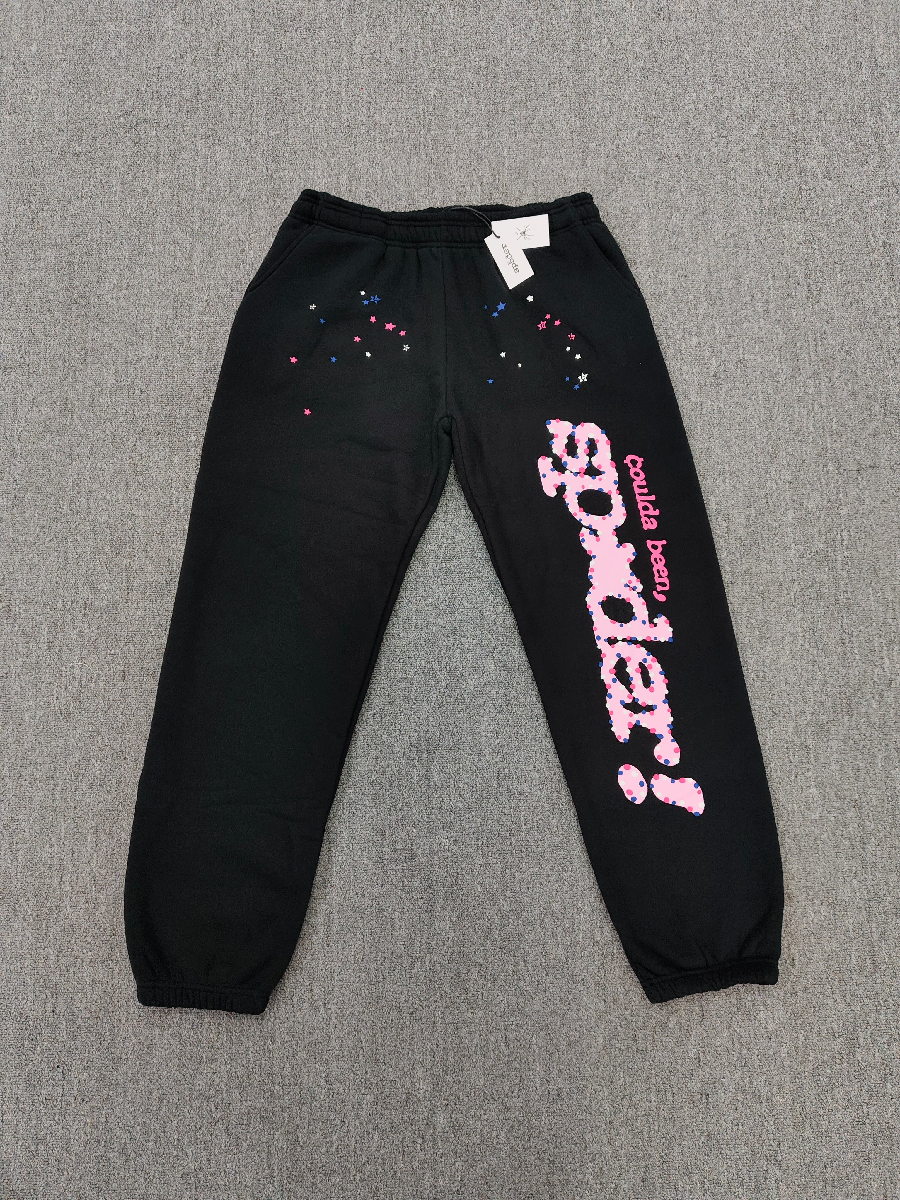 black Sp5der x Coulda Been sweatpants featuring a prominent pink "spider!" graphic and multi-colored star embroidery