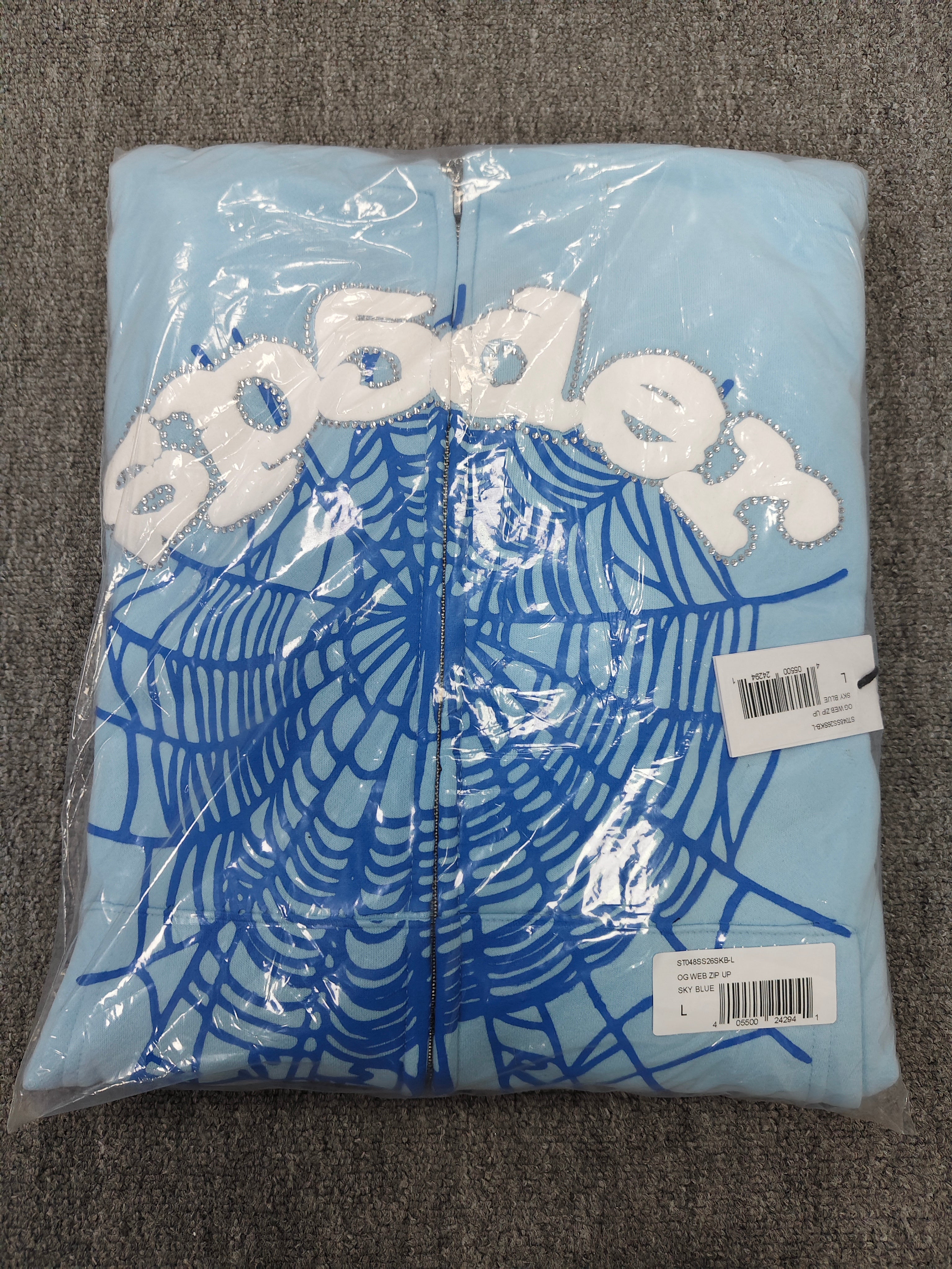 Sp5der OG Web Zip Up hoodie in Sky Blue features a prominent 3D puff-printed spider web graphic and rhinestone embellishments