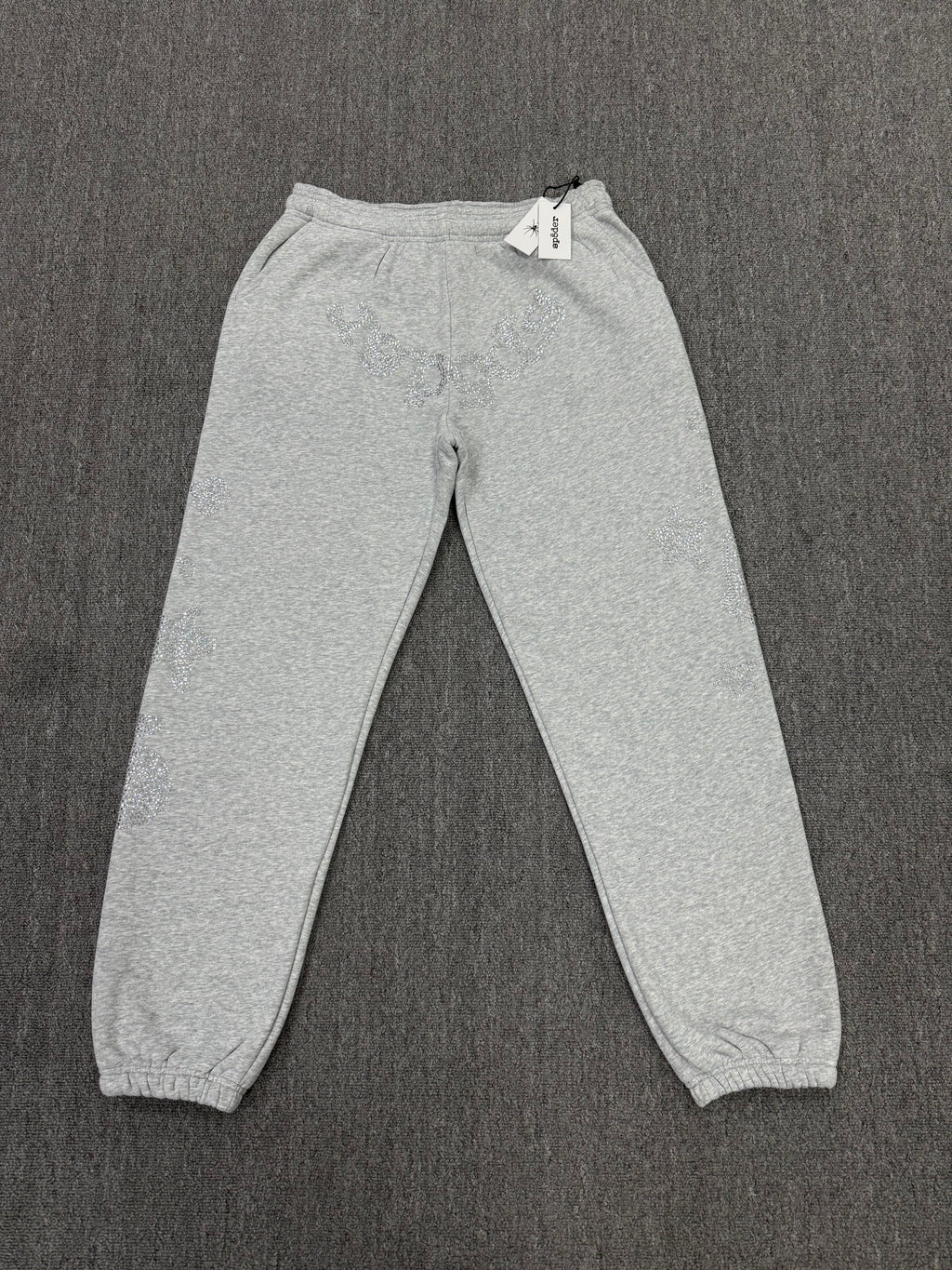 light grey sp5der joggers feature a unique rhinestone across the front hip area