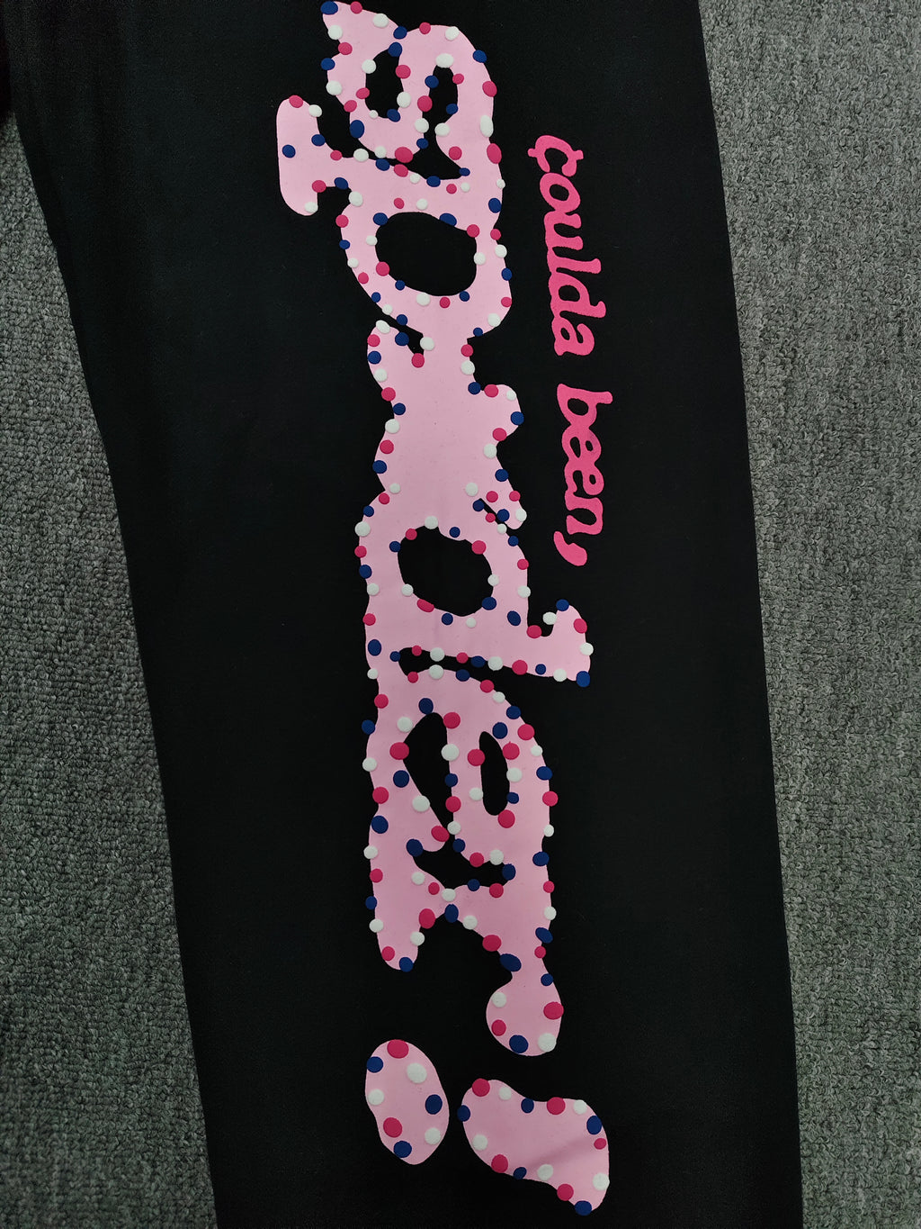 black Sp5der x Coulda Been sweatpants featuring a prominent pink "spider!" graphic and multi-colored star embroidery