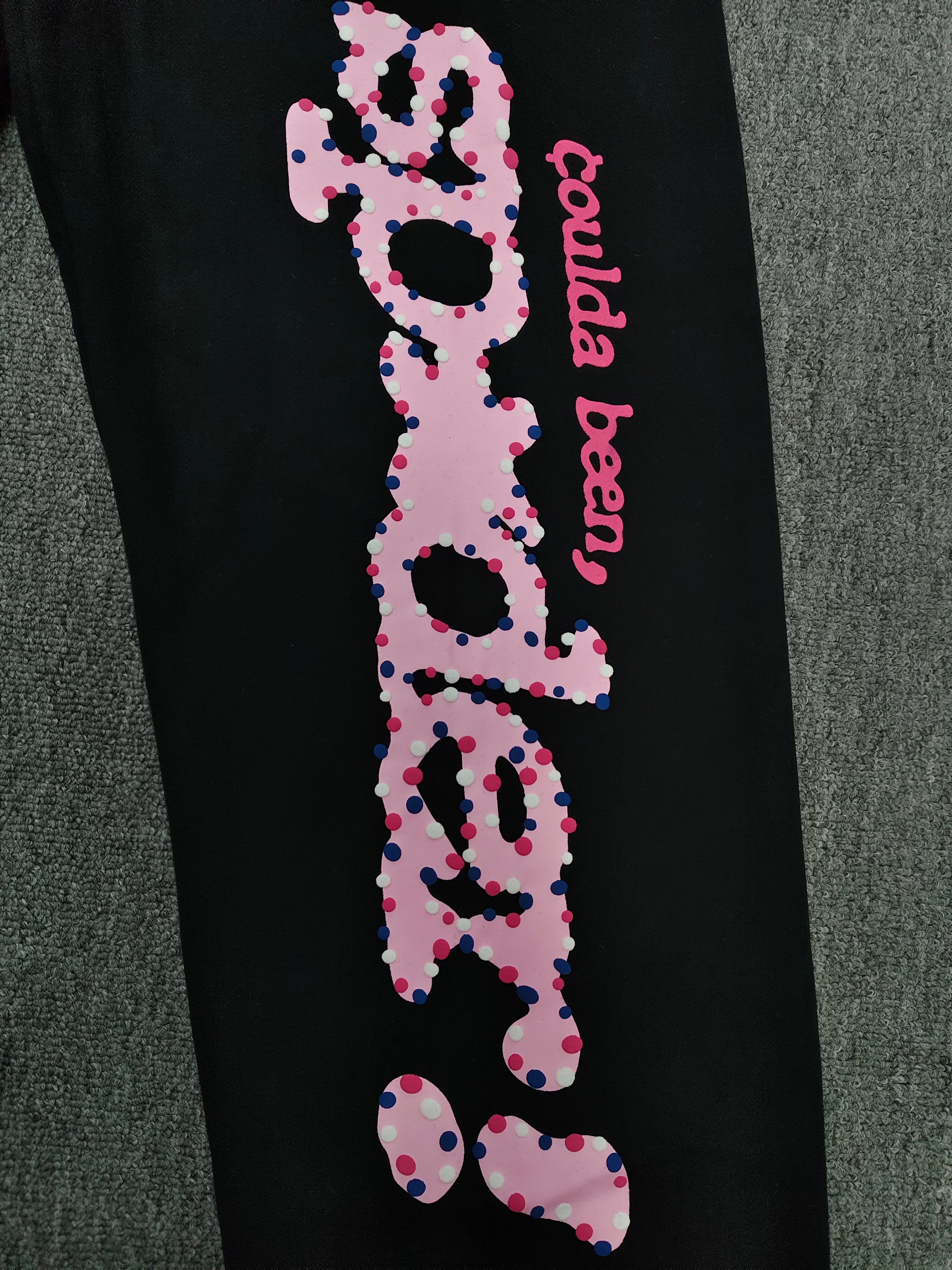 black Sp5der x Coulda Been sweatpants featuring a prominent pink "spider!" graphic and multi-colored star embroidery