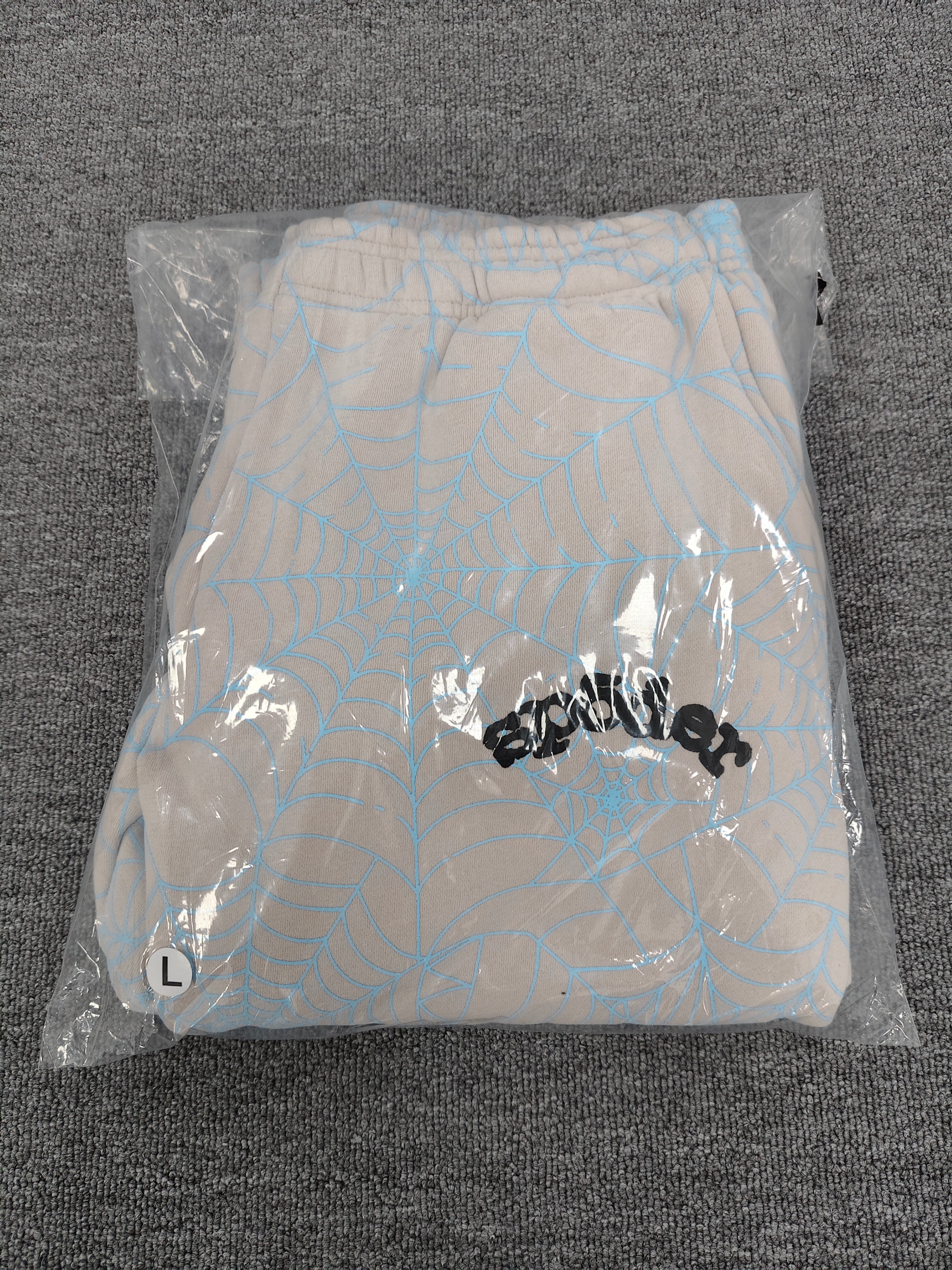 Sp5der AOP Web Heather Grey Sweatpants featuring a distinctive all-over blue spiderweb print and a contrasting black logo on the thigh.