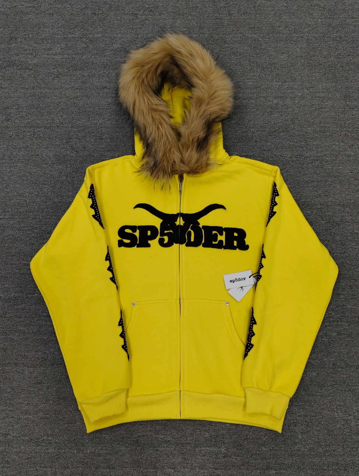 a yellow Sp5der fur-hooded zip-up sweatshirt featuring a prominent black logo and studded sleeve details