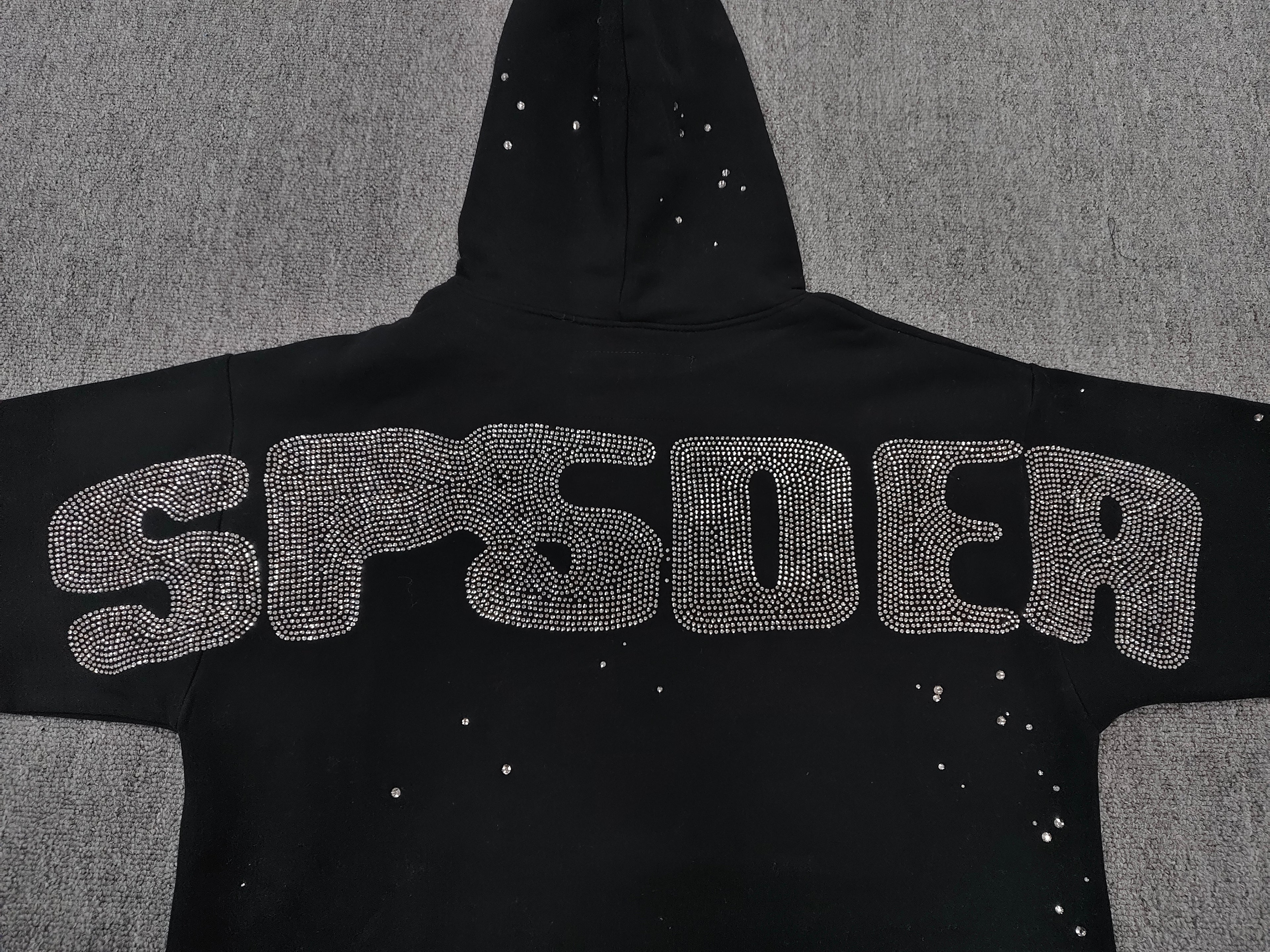 a Sp5der Rhinestone Silk Hoodie in black, featuring a prominent rhinestone web graphic on the front