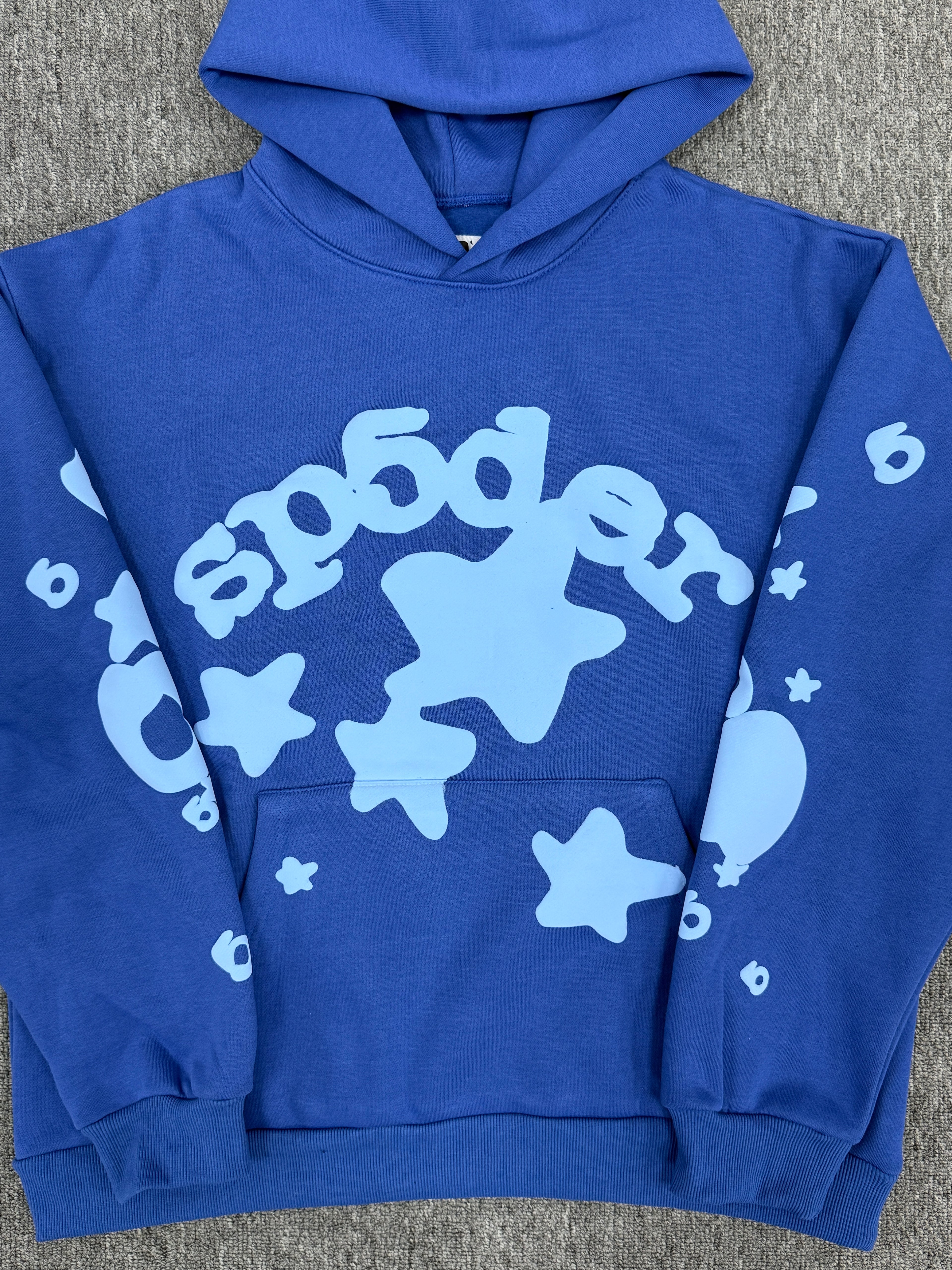 blue Sp5der Beluga hoodie features a distinct light blue graphic print of stars and the brand name on the front and sleeves