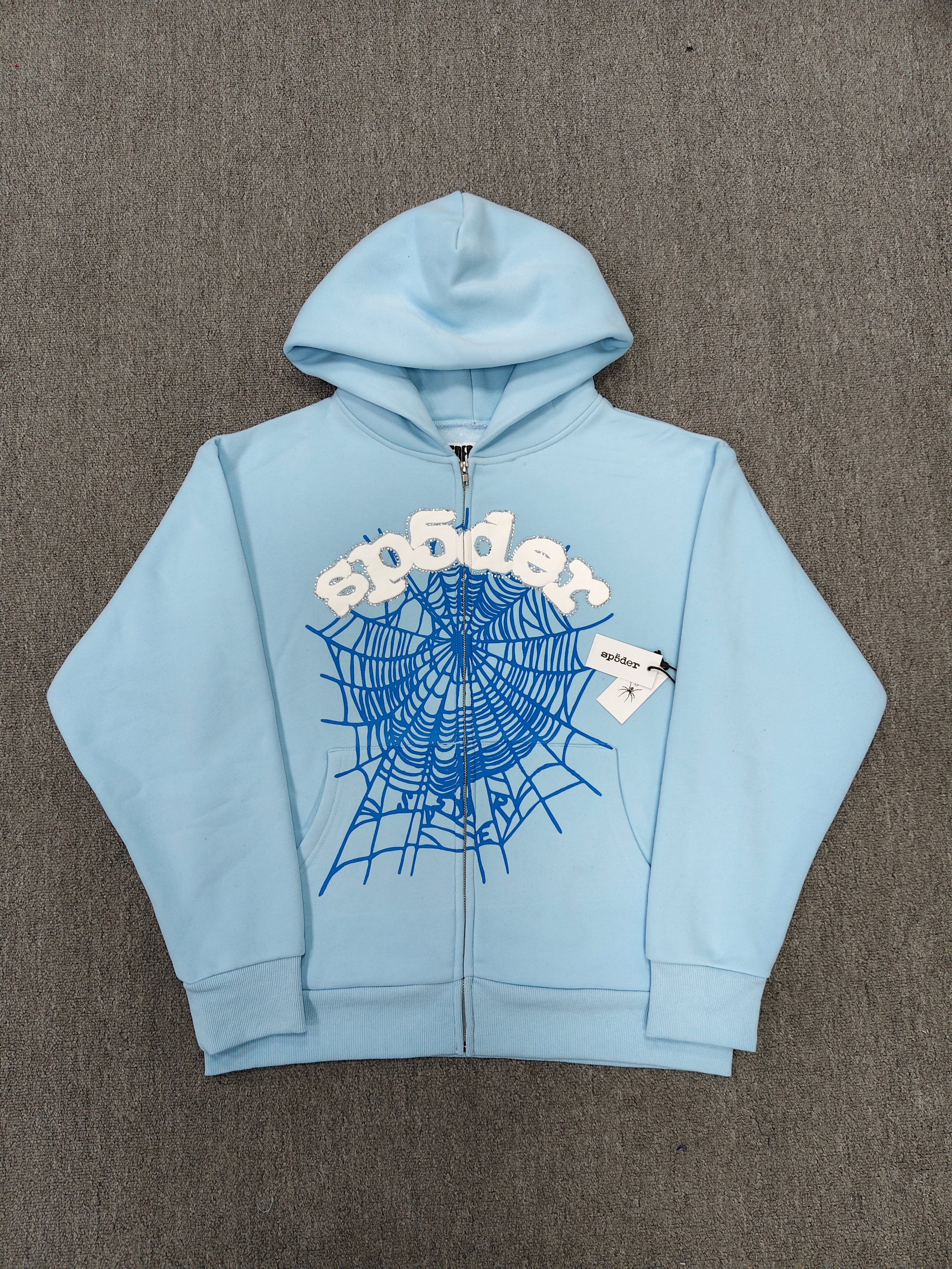 Sp5der OG Web Zip Up hoodie in Sky Blue features a prominent 3D puff-printed spider web graphic and rhinestone embellishments