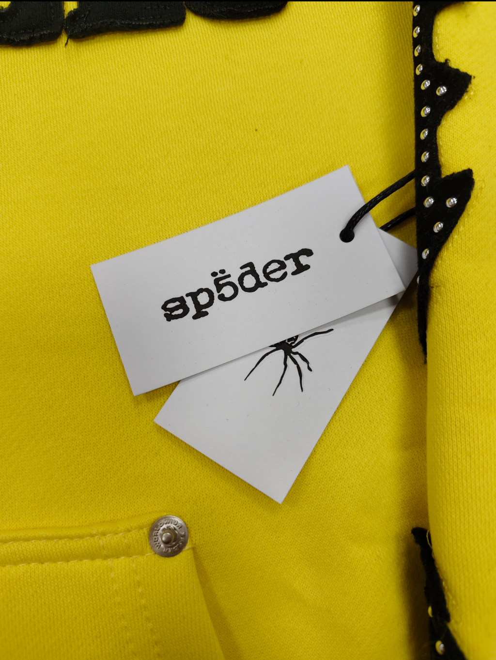 a yellow Sp5der fur-hooded zip-up sweatshirt featuring a prominent black logo and studded sleeve details