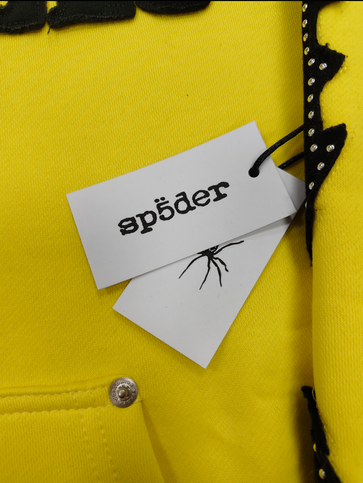 a yellow Sp5der fur-hooded zip-up sweatshirt featuring a prominent black logo and studded sleeve details