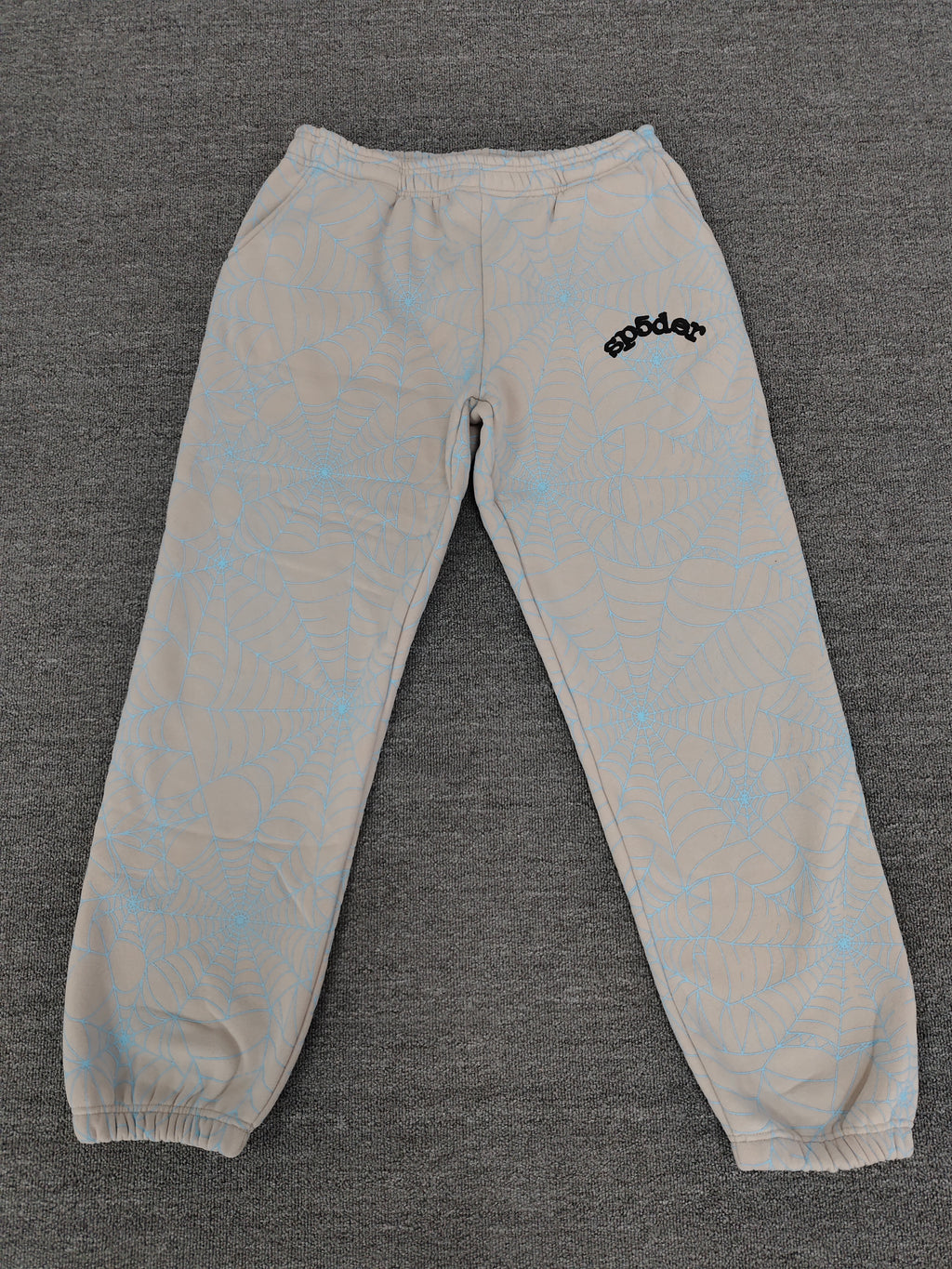 Sp5der AOP Web Heather Grey Sweatpants featuring a distinctive all-over blue spiderweb print and a contrasting black logo on the thigh.
