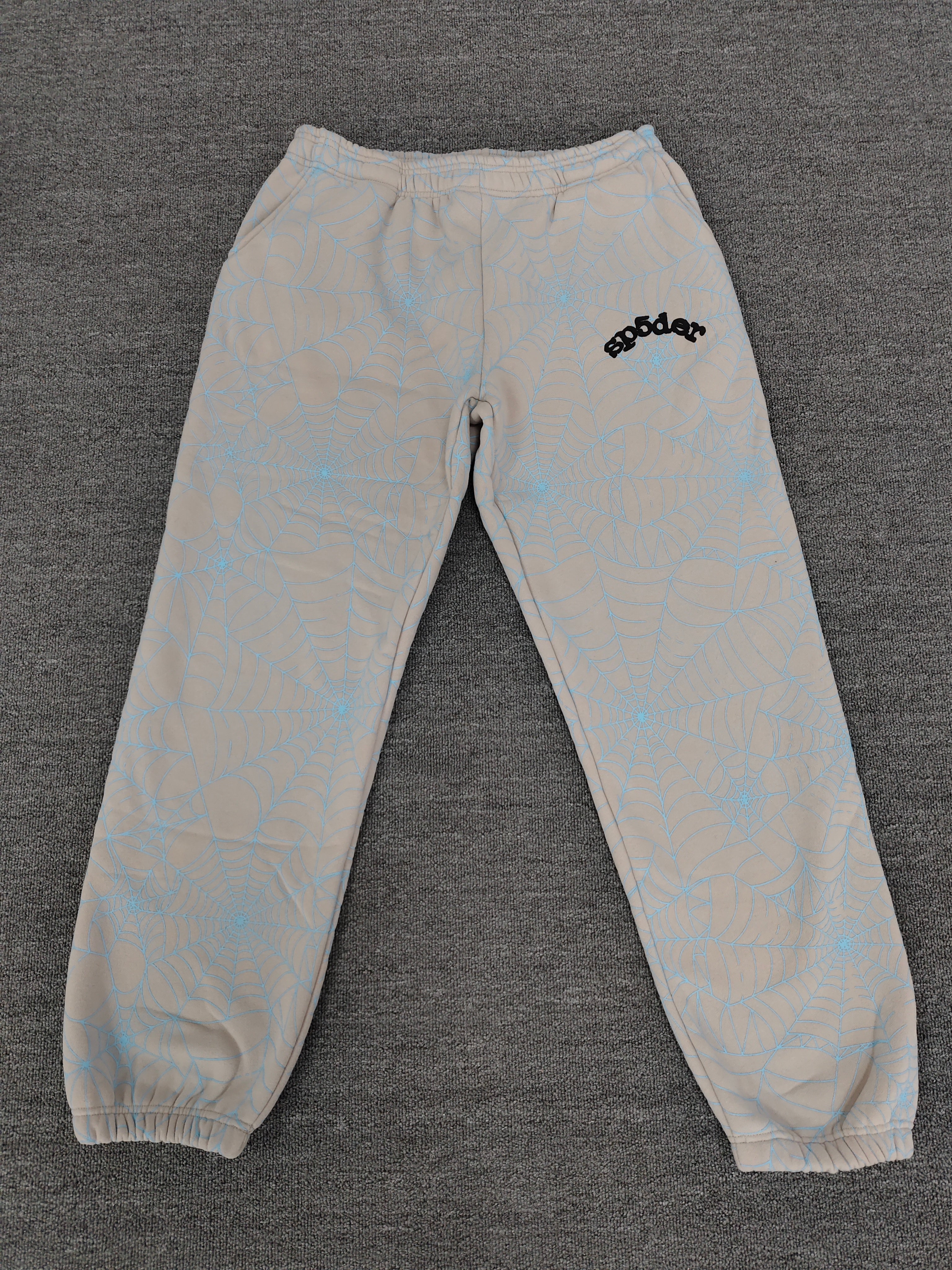 Sp5der AOP Web Heather Grey Sweatpants featuring a distinctive all-over blue spiderweb print and a contrasting black logo on the thigh.