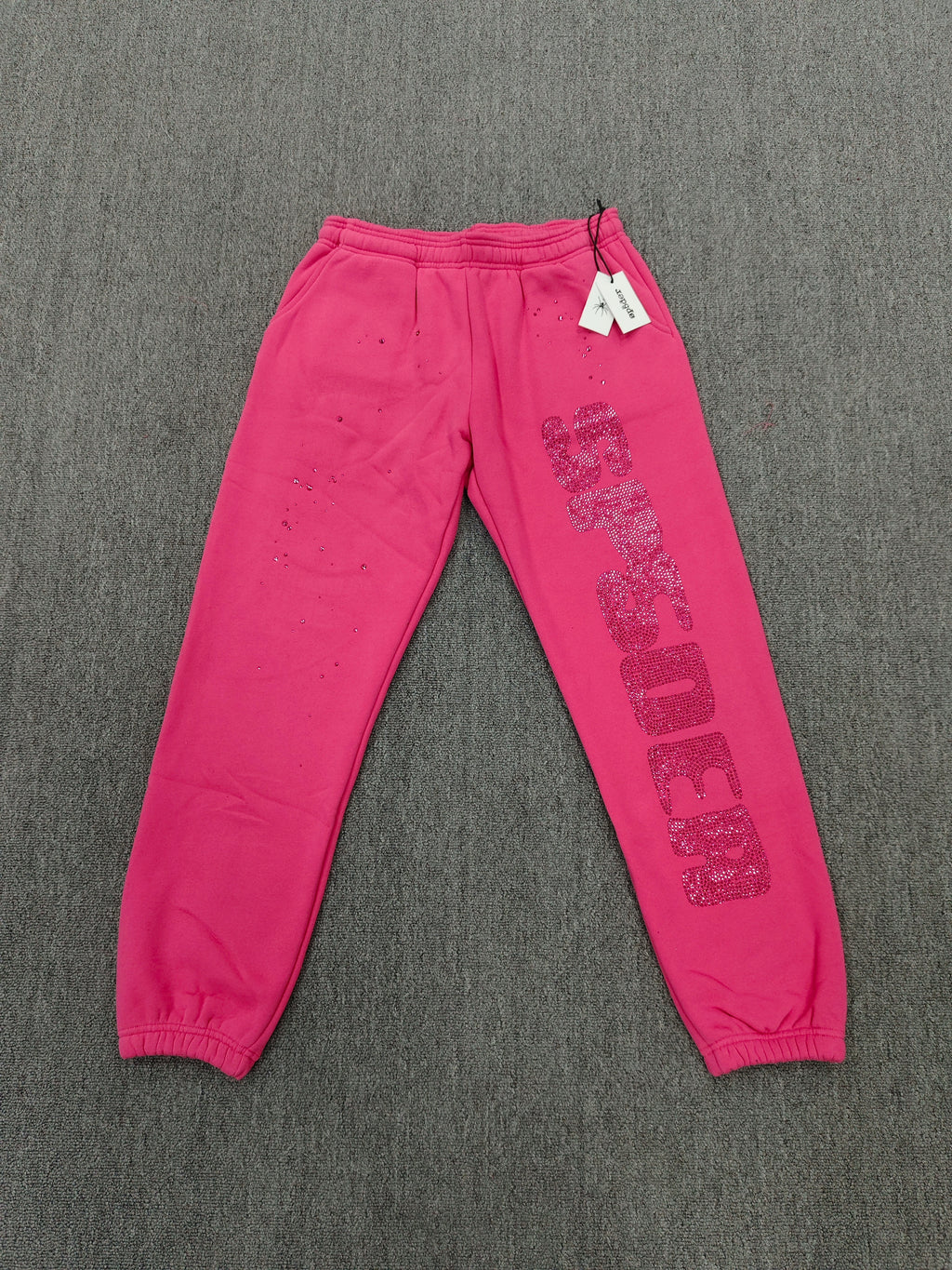 pink Sp5der sweatpants feature rhinestone branding down the leg and are identified as the Rhinestone Silk Sweatpant model