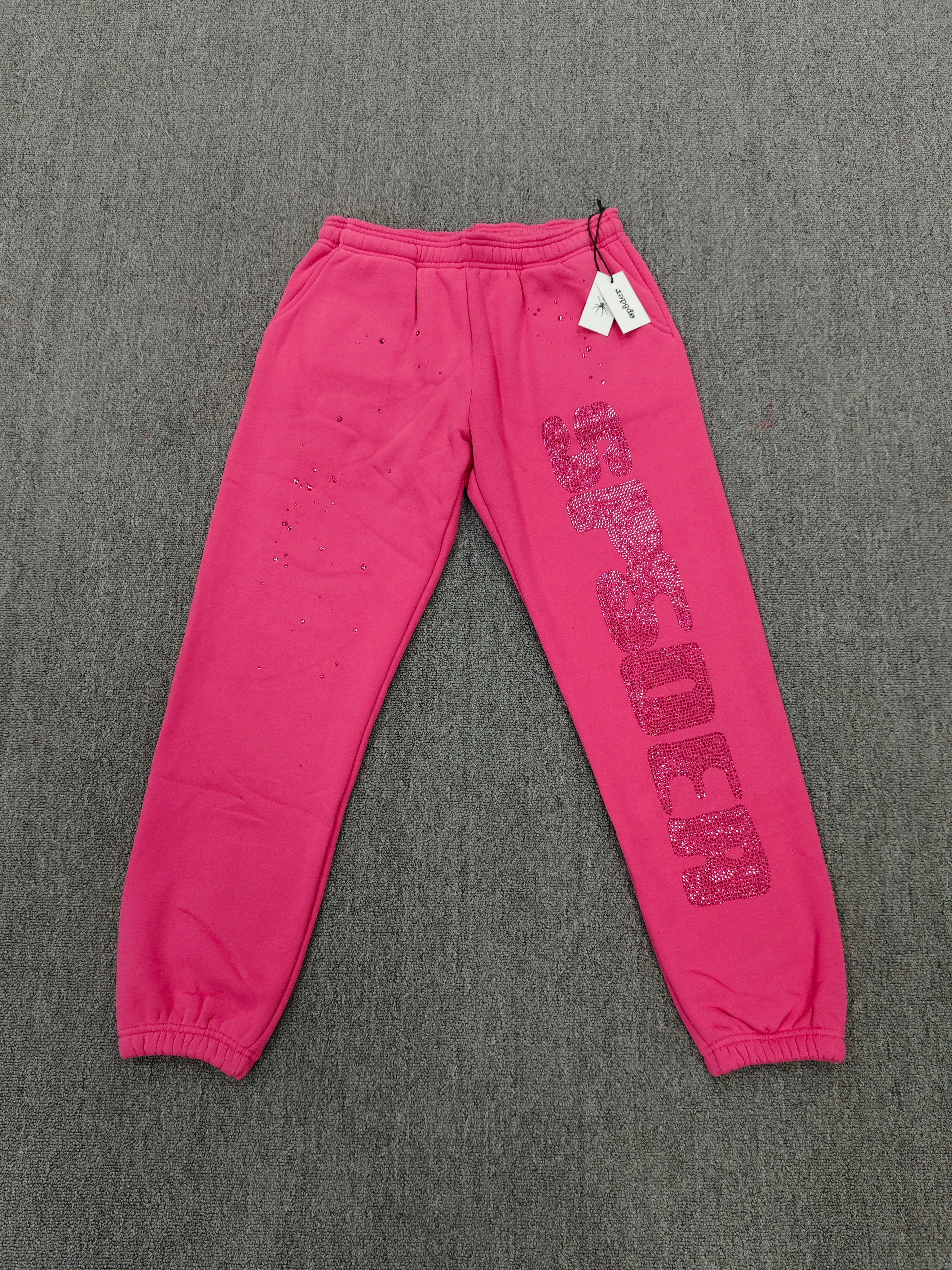 pink Sp5der sweatpants feature rhinestone branding down the leg and are identified as the Rhinestone Silk Sweatpant model