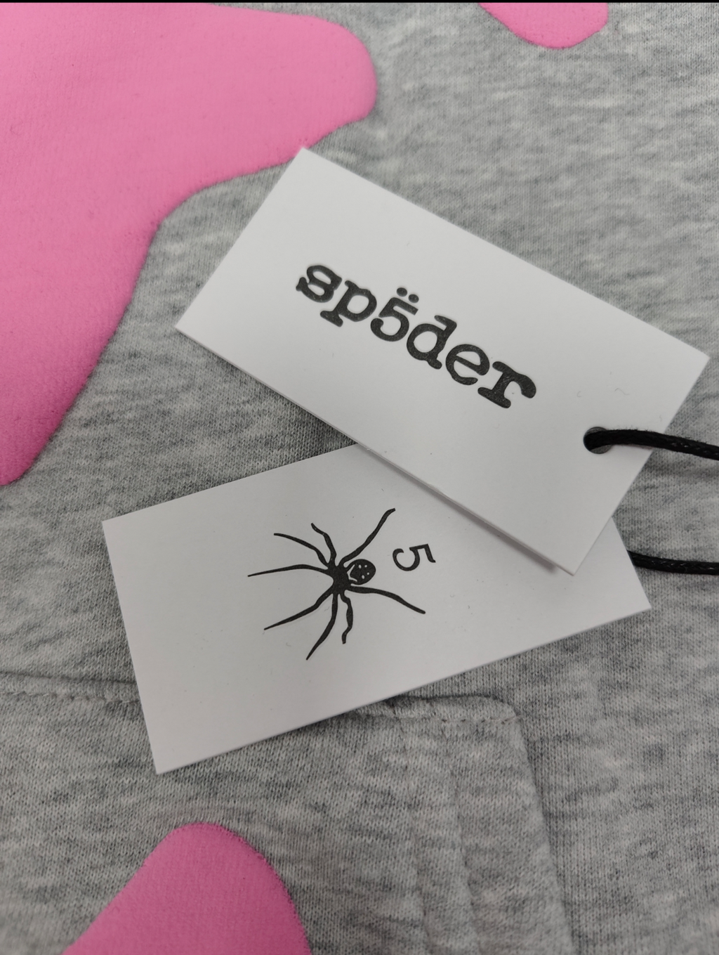 a grey Sp5der "Beluga" hoodie featuring pink star graphics and brand lettering
