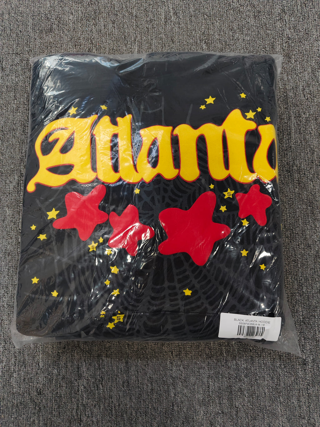 black SP5DER Atlanta hoodie features yellow lettering, red stars, and a spiderweb graphic