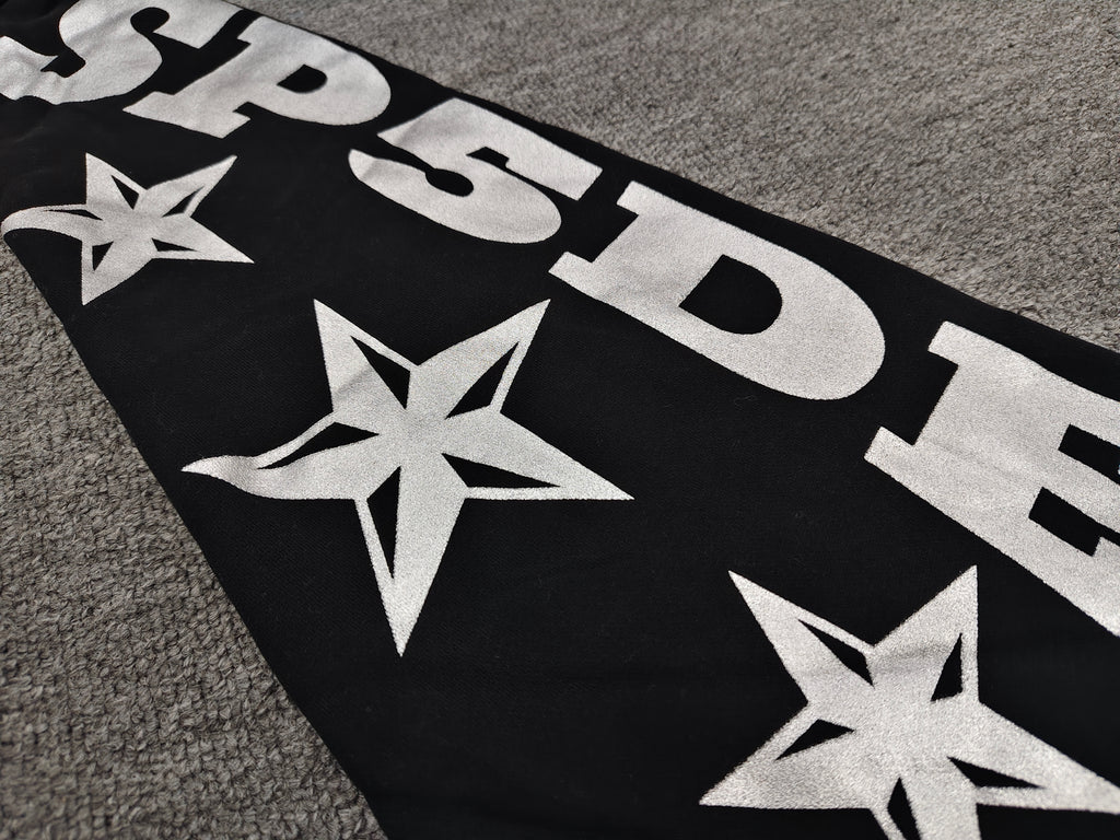 a Sp5der MX555 Zip Hoodie in black, featuring white graphic lettering and star prints on the sleeves