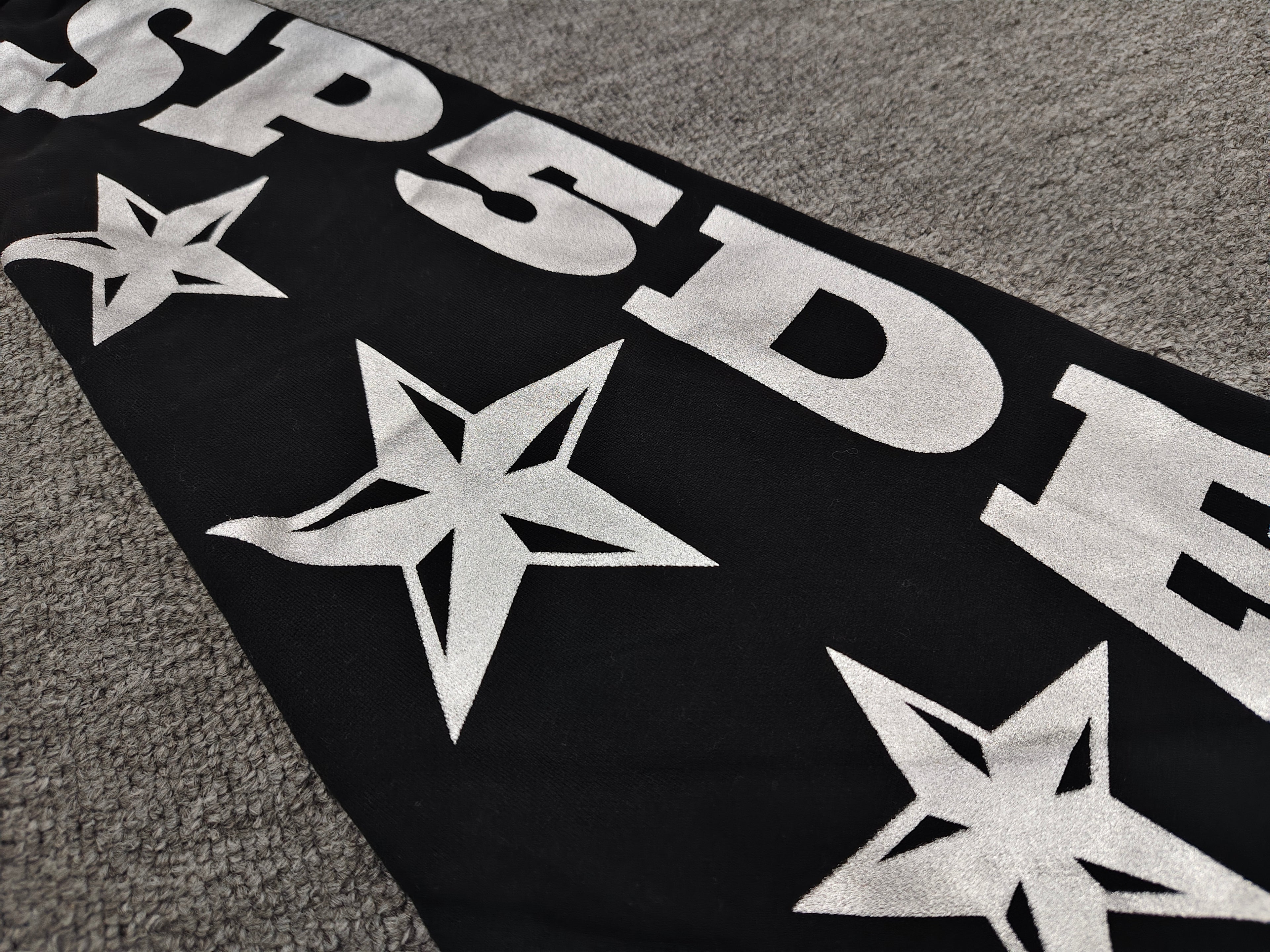 a Sp5der MX555 Zip Hoodie in black, featuring white graphic lettering and star prints on the sleeves