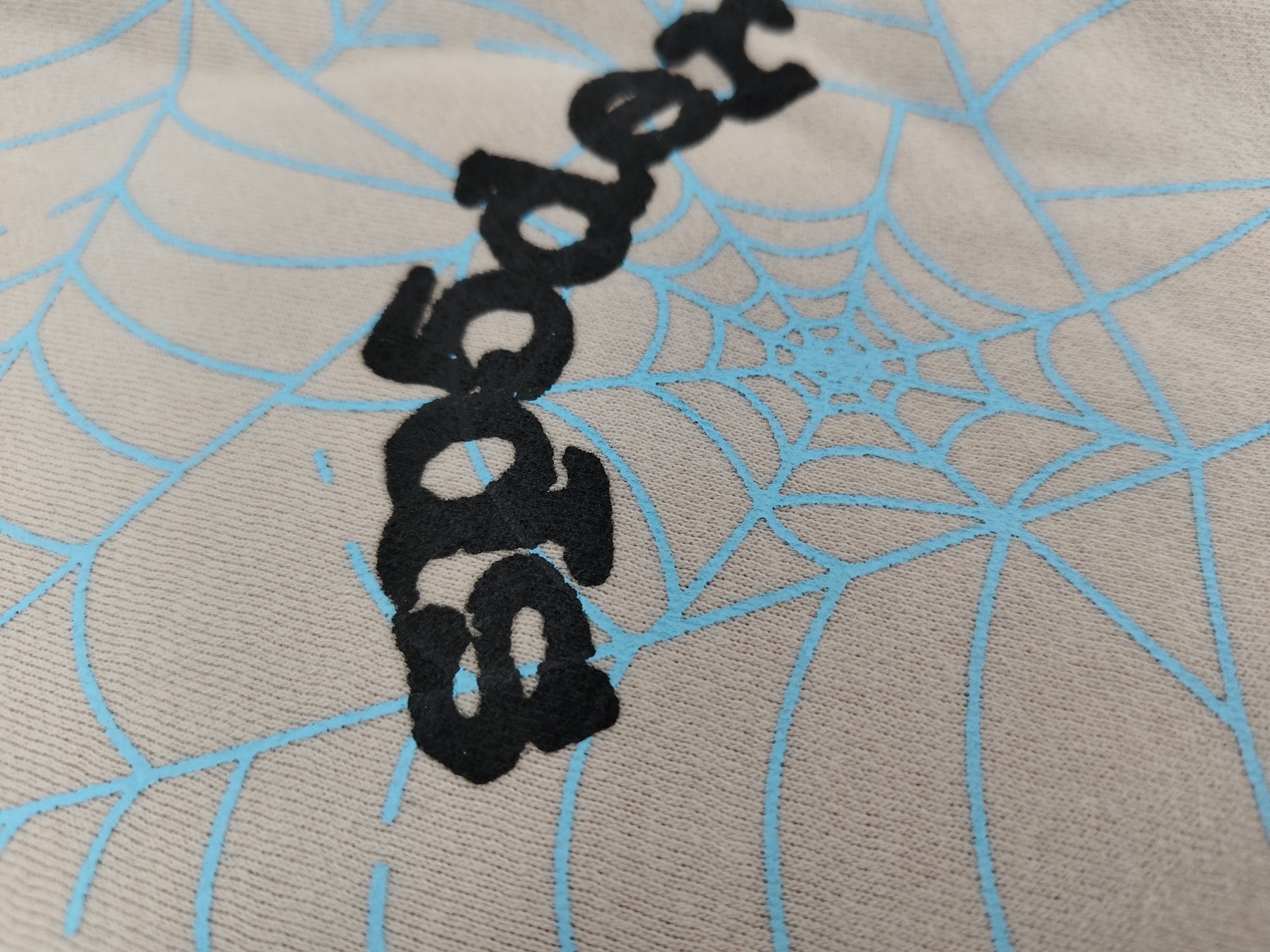 Sp5der AOP Web Heather Grey Sweatpants featuring a distinctive all-over blue spiderweb print and a contrasting black logo on the thigh.