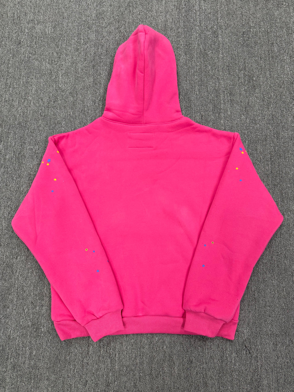 pink Sp5der graphic-print hoodie features a black spiderweb design on the front with scattered multicolored stars
