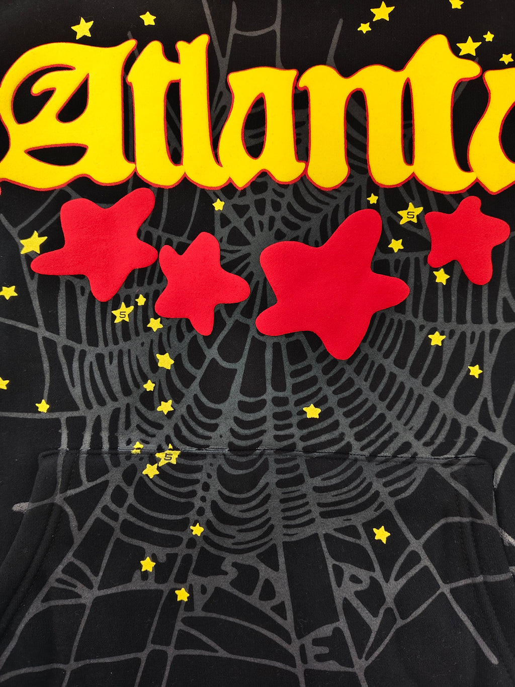 black SP5DER Atlanta hoodie features yellow lettering, red stars, and a spiderweb graphic